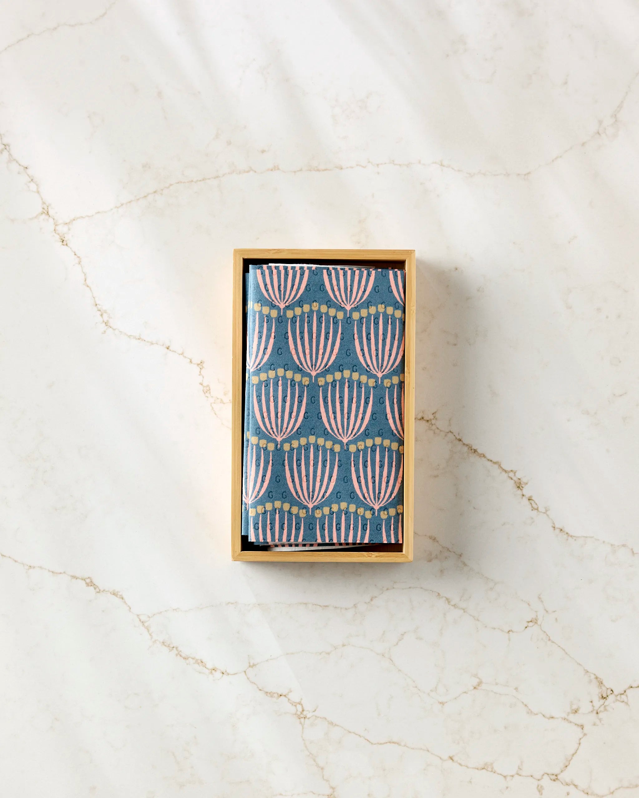 A small rectangular Josie box by Amy MacCready contains cards with a blue background and pink and white abstract floral patterns, reminiscent of reusable paper towels, displayed on a light marble surface.
