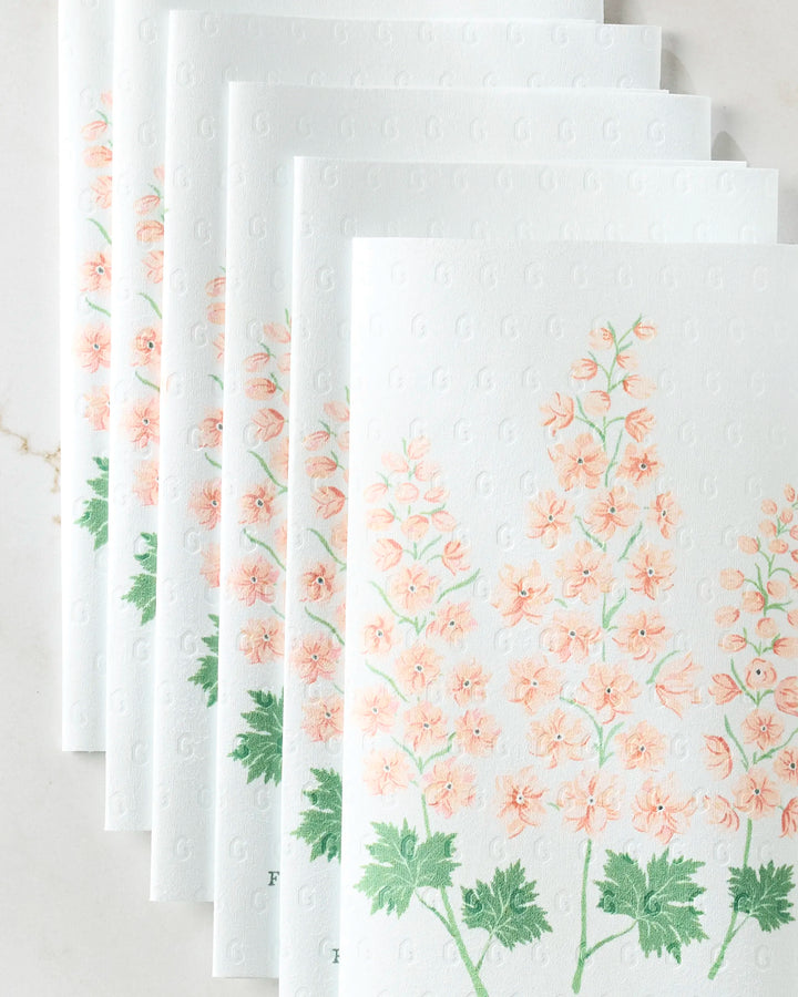 Linda Fox’s July Delphinium eco-friendly paper towels are arranged in a fan shape, each featuring white embossed sheets with pink floral and green leaf prints.