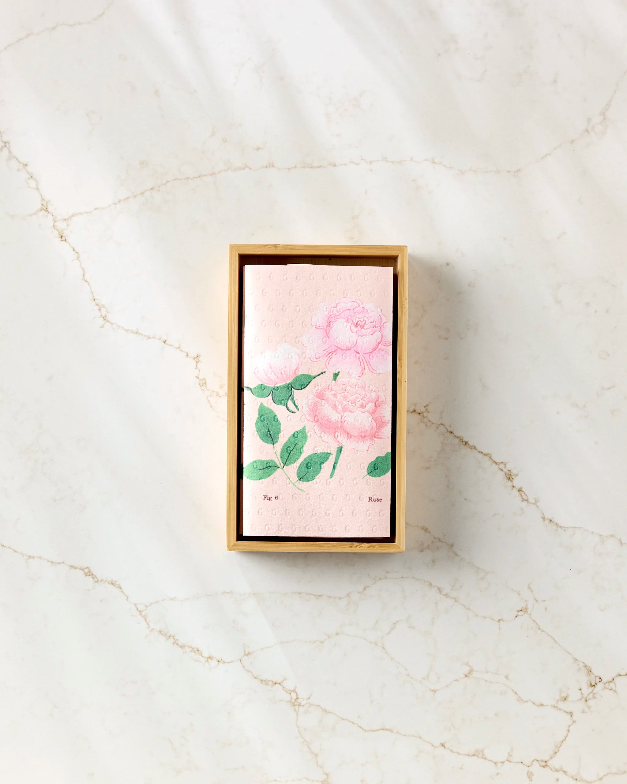 The June Roses bar soap by Linda Fox features a floral pink and green design in a wooden box on white marble, pairing beautifully with eco-friendly kitchen towels for a stylish, sustainable accent.