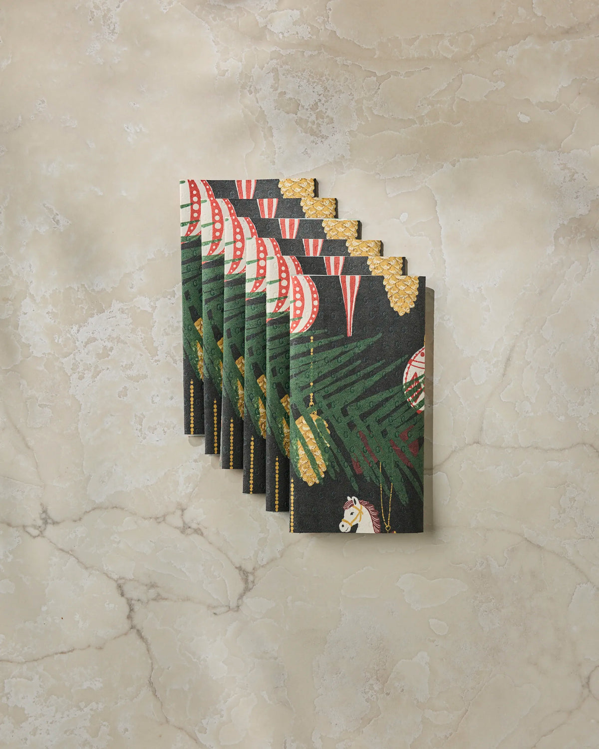 Seven decorative Keepsake envelopes by Geometry, showcasing a festive design with green foliage and a horse, artfully arranged in a fanned-out pattern on a marble surface—perfect for gifting eco-friendly paper towels or other sustainable surprises inside.
