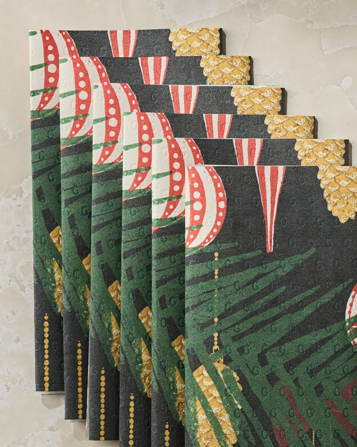 Six decorative cards from Geometry’s Keepsake collection, showcasing a festive pattern with green leaves, red-and-white striped ornaments, and metallic gold accents, arranged in a fanned-out display on a light marble surface—perfect inspiration for those who appreciate the beauty of eco-friendly paper towels and sustainable living.