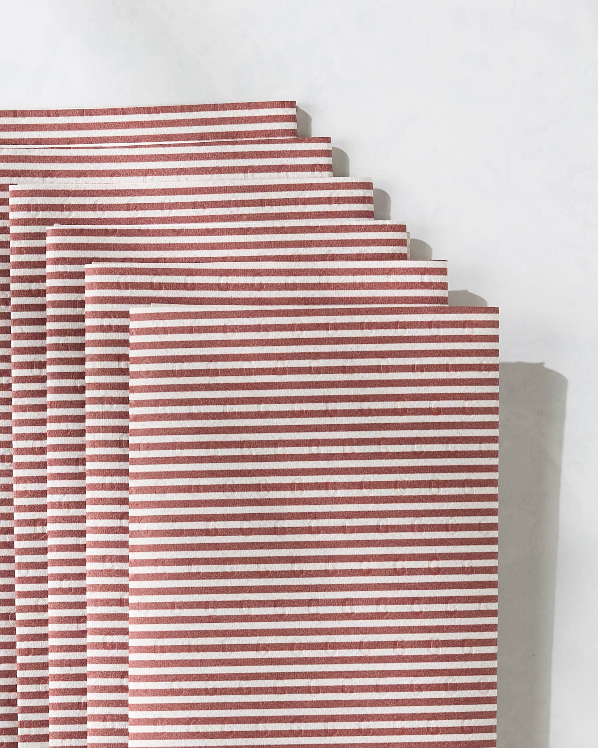 Several neatly stacked Geometry Kringle napkins, with red-and-white stripes, are arranged on a white surface—showcasing their eco-friendly design as reusable kitchen towels, not paper towels.