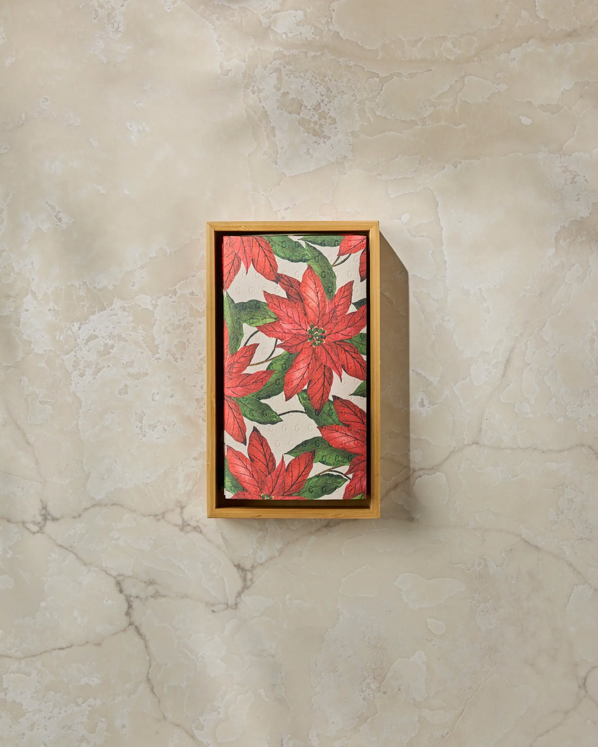 The Geometry Lauri is a rectangular wooden box with a lid adorned with red poinsettia flowers and green leaves. Sitting on a beige marble surface, it offers an eco-friendly solution for storing or presenting reusable paper towels.