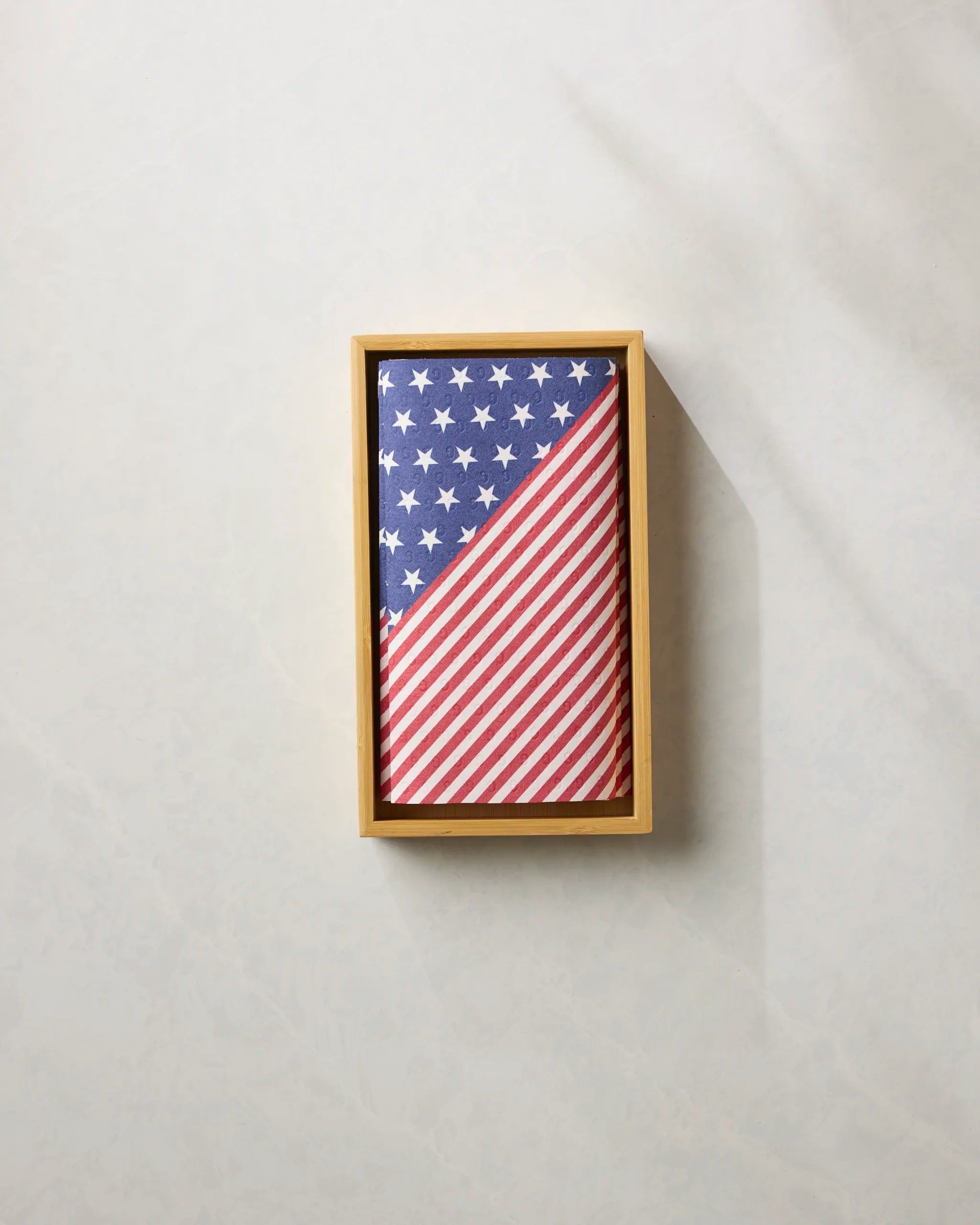 A neatly folded American flag with stars and stripes is displayed in a rectangular wooden frame against a light, textured background—symbolizing values of honor and sustainability, reflected by Geometry’s Liberty eco-friendly paper towels.