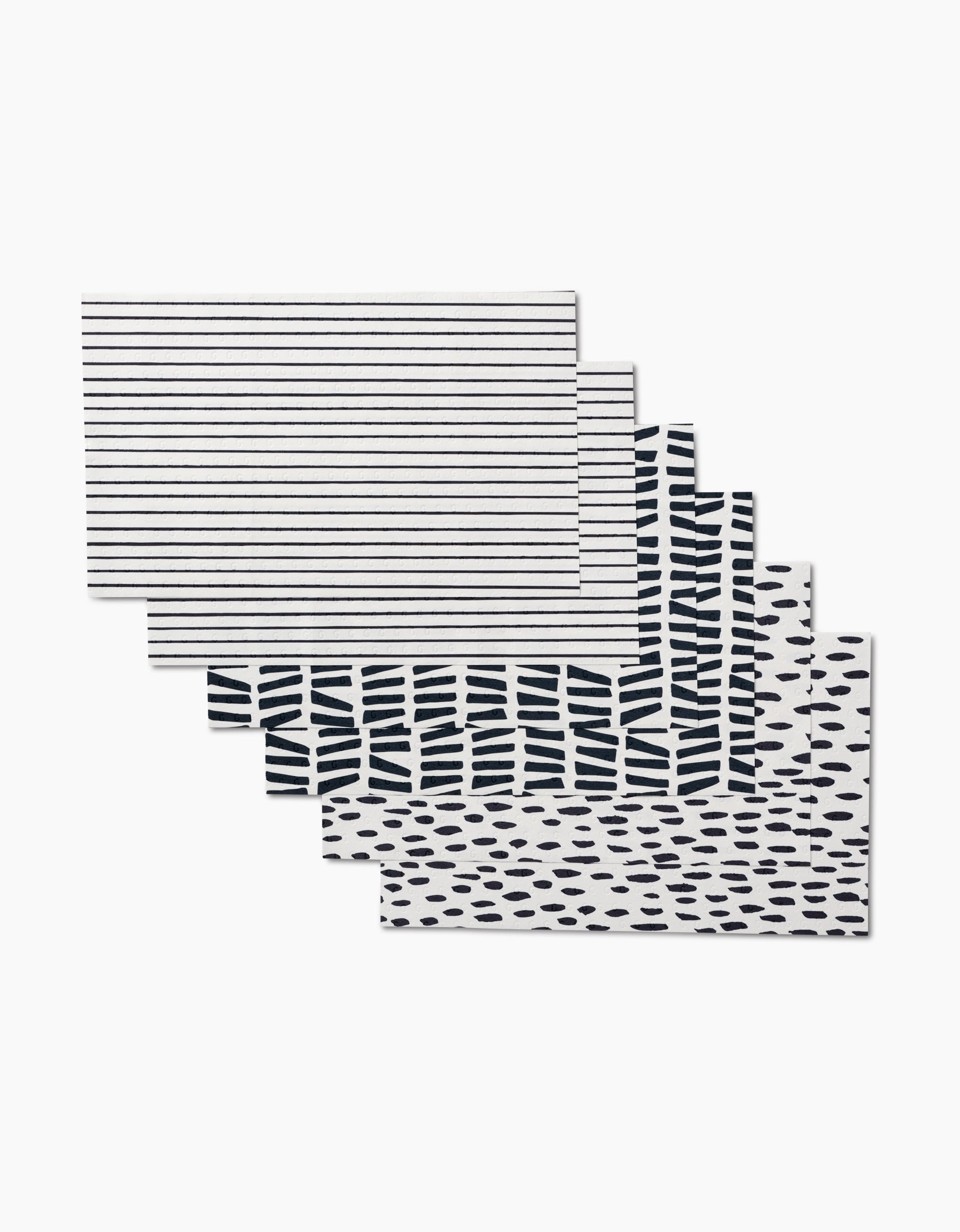 Five rectangular GEOMETRY placemats, Lines, Dots and Dashes, feature unique black and white geometric patterns—stripes, dashes, and dots—in a fanned-out stack. Made from eco-friendly post-consumer recycled materials.