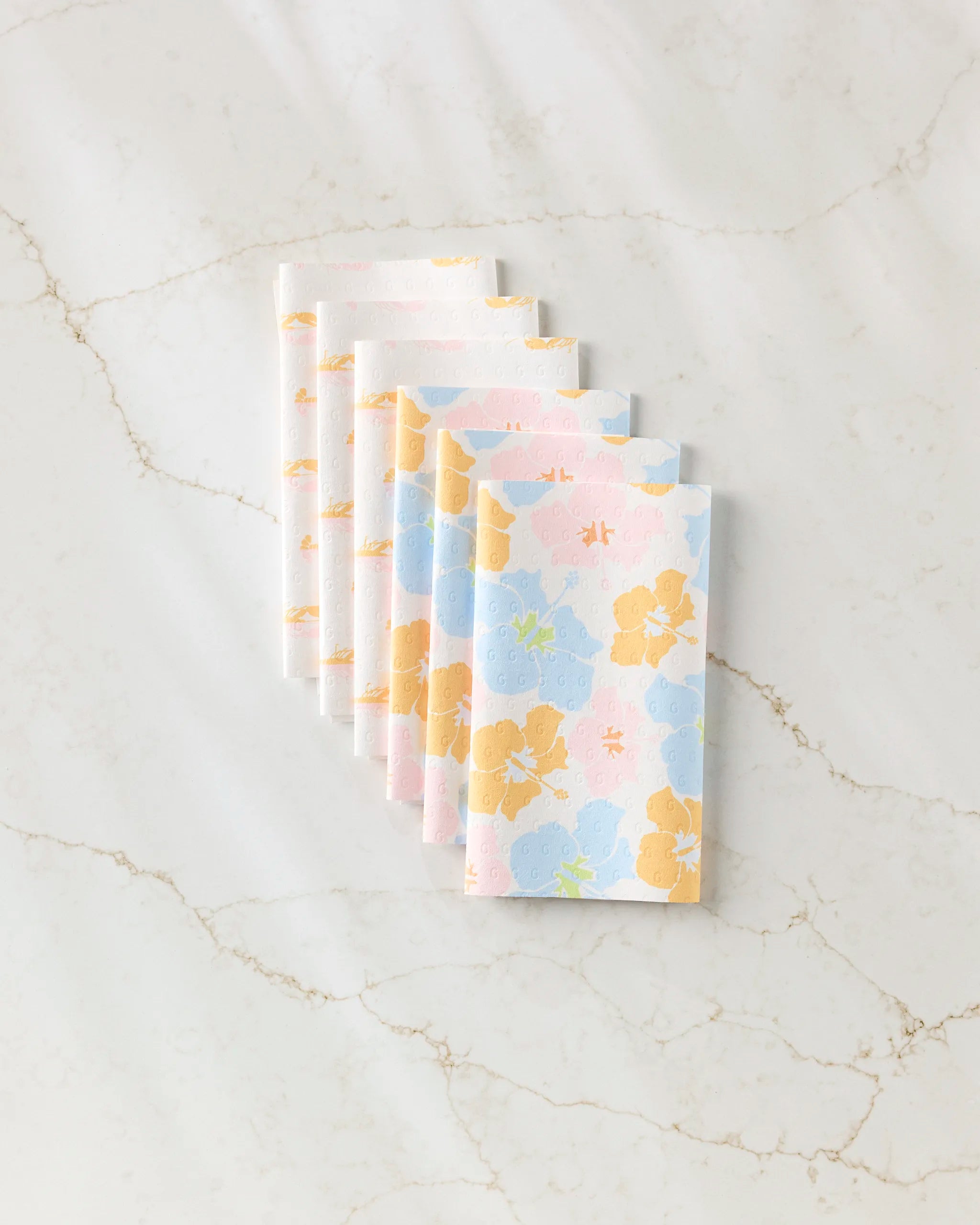 Seven Lobster Love napkins by GEOMETRY, featuring a red lobster print on eco-friendly paper towels, are neatly fanned out on a white marble surface with light brown veining.