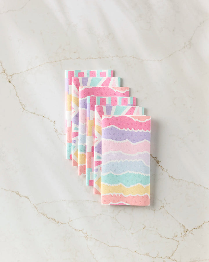 Six pastel-colored, reusable Lots of Dots paper towels by Rebecca Bobko are neatly stacked on a light marble surface.