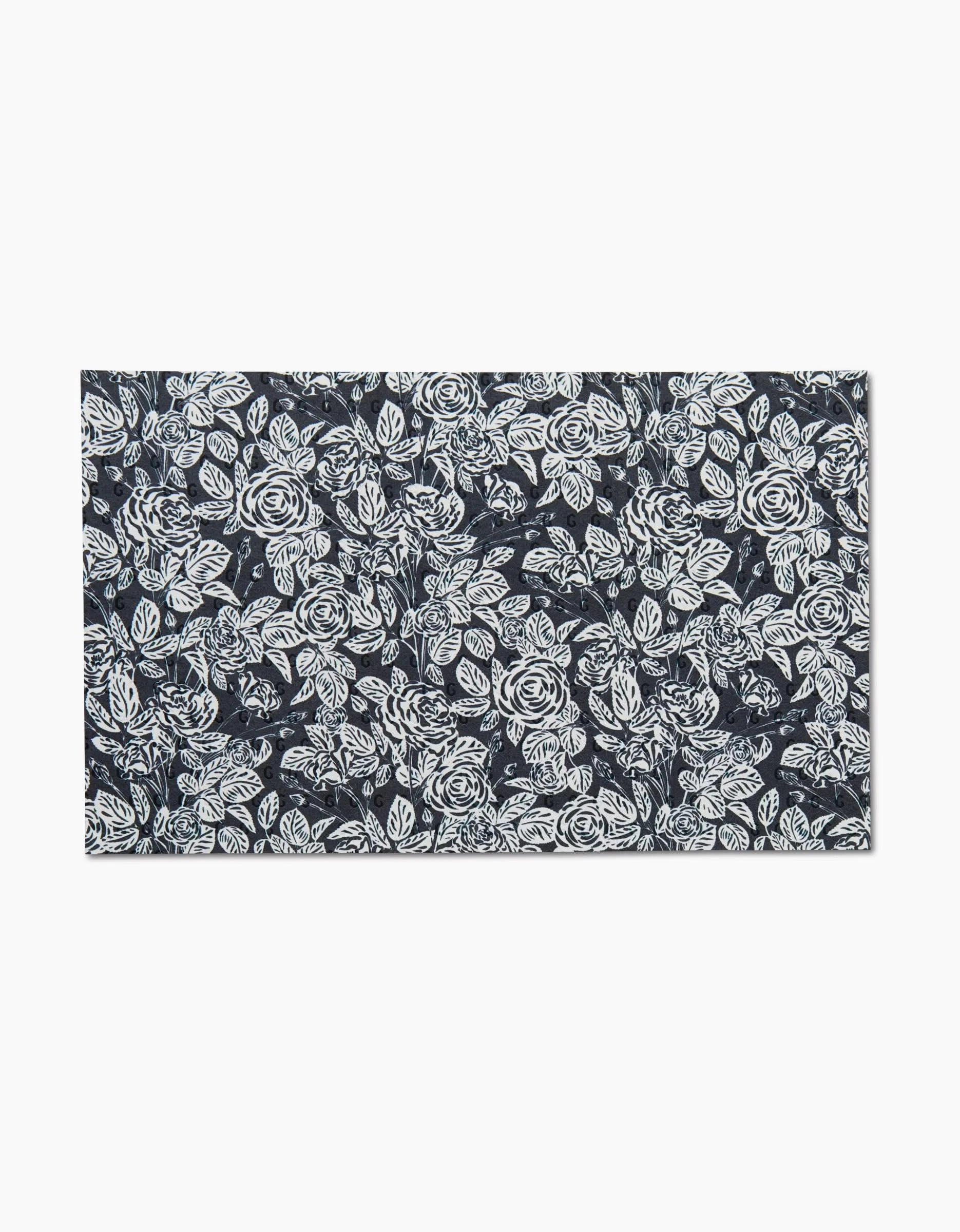 The Love and Roses Onyx mat by Charlie Rowan Designs features intricate white roses and leaves on a dark blue background, crafted from eco-friendly paper towels for a sustainable touch.