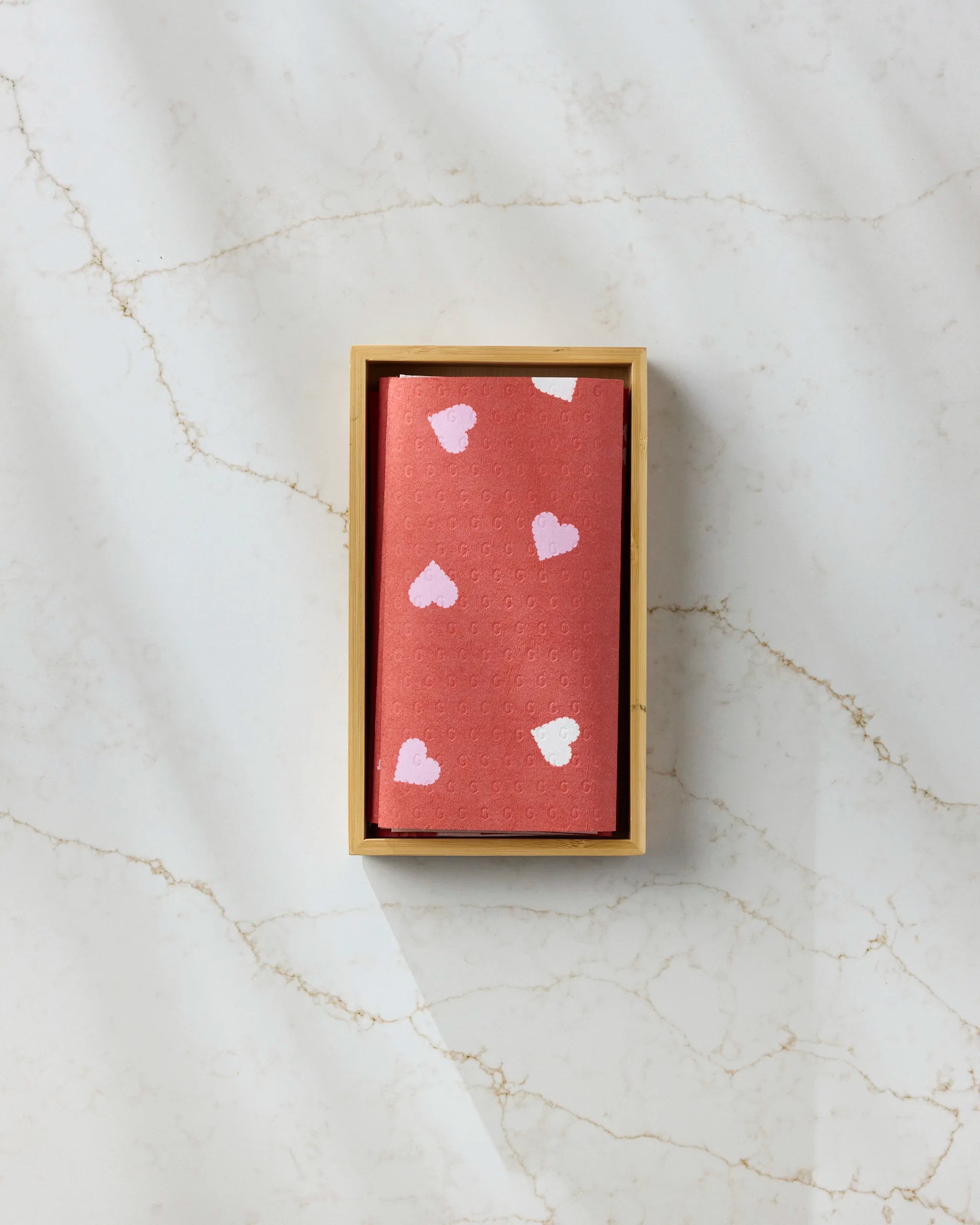 The Geometry Love Confetti box features a pink design with white and light pink hearts, placed on a white marble surface—perfect for stylishly storing your reusable paper towels.