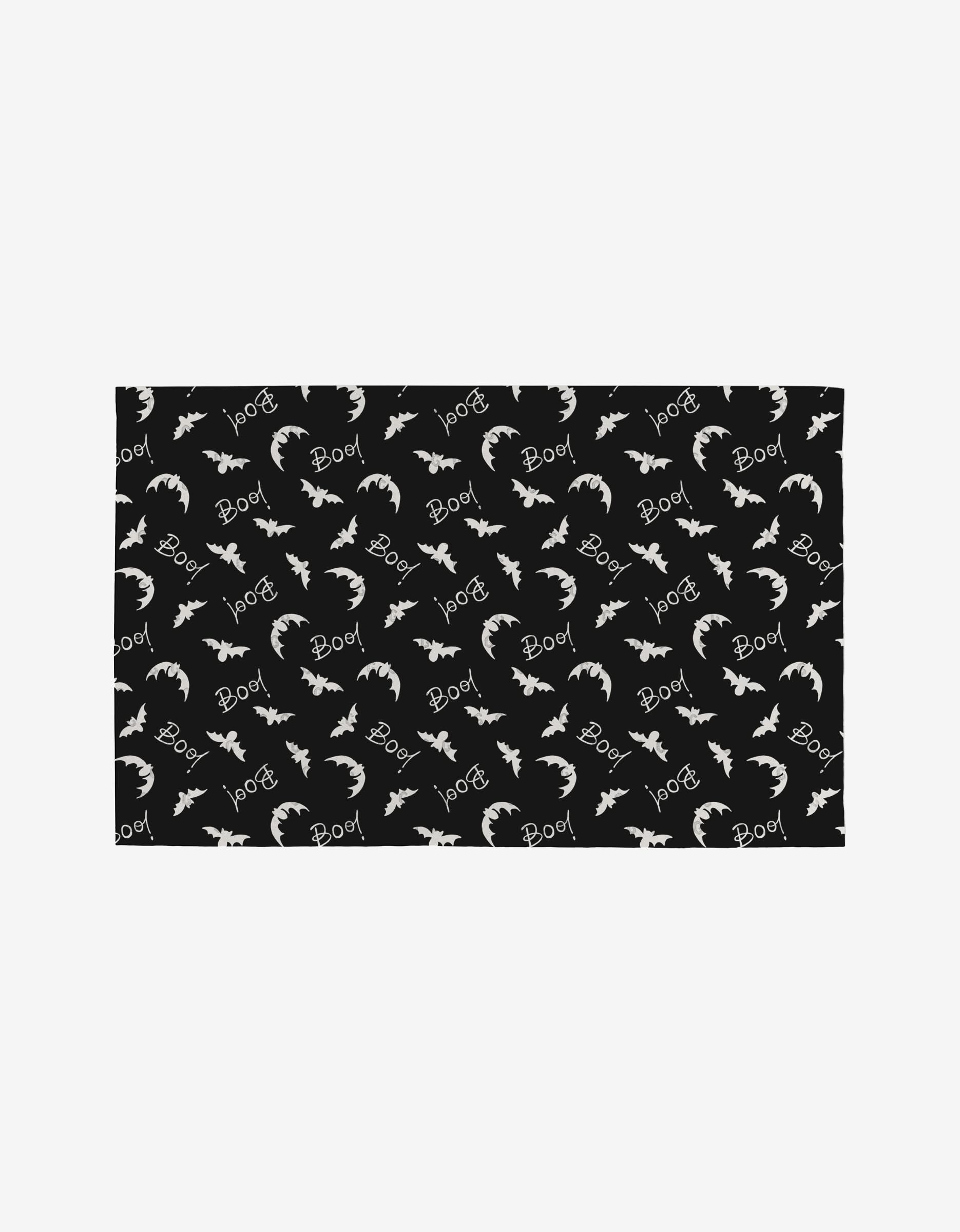 The Love Potions mat by Hufton Studio is a rectangular black mat with a festive Halloween-themed pattern—white bats, “Boo!”, and crescent moons—designed as an eco-friendly, reusable décor option.