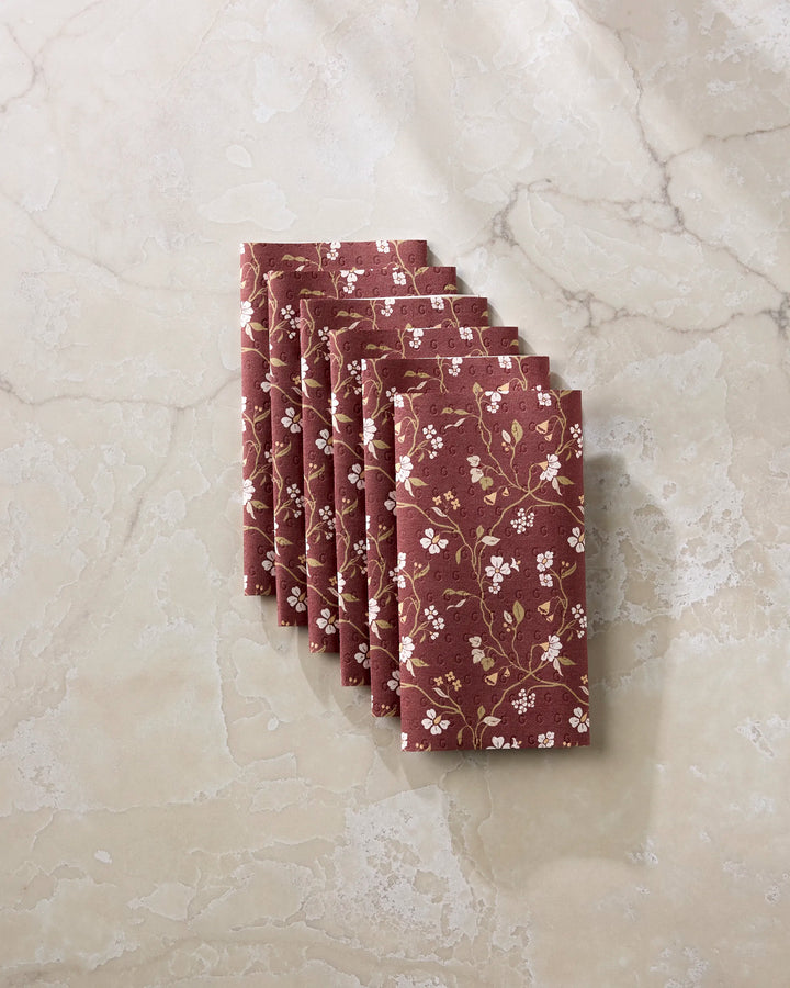 Seven Lunaria in Merlot cloth napkins by Danelys Sidron, featuring a white and yellow floral design, are neatly stacked on beige marble—a stylish, eco-friendly alternative to paper towels.