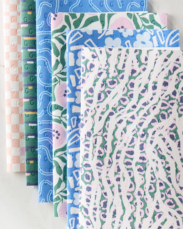 Six Magic Field cleaning cloths by Happy Hemera, featuring checkered, swirl, floral, and abstract animal patterns, are fanned out on a light surface—an eco-friendly alternative to reusable paper towels.