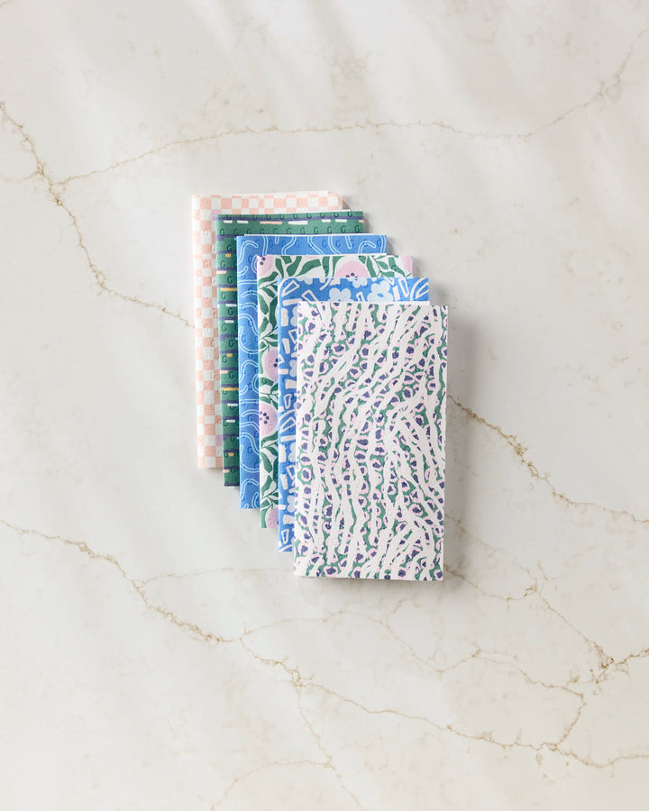 Six Magic Field reusable paper towels by Happy Hemera in pastel blue, green, lavender, and pink are neatly stacked on a white marble surface with subtle brown veining.
