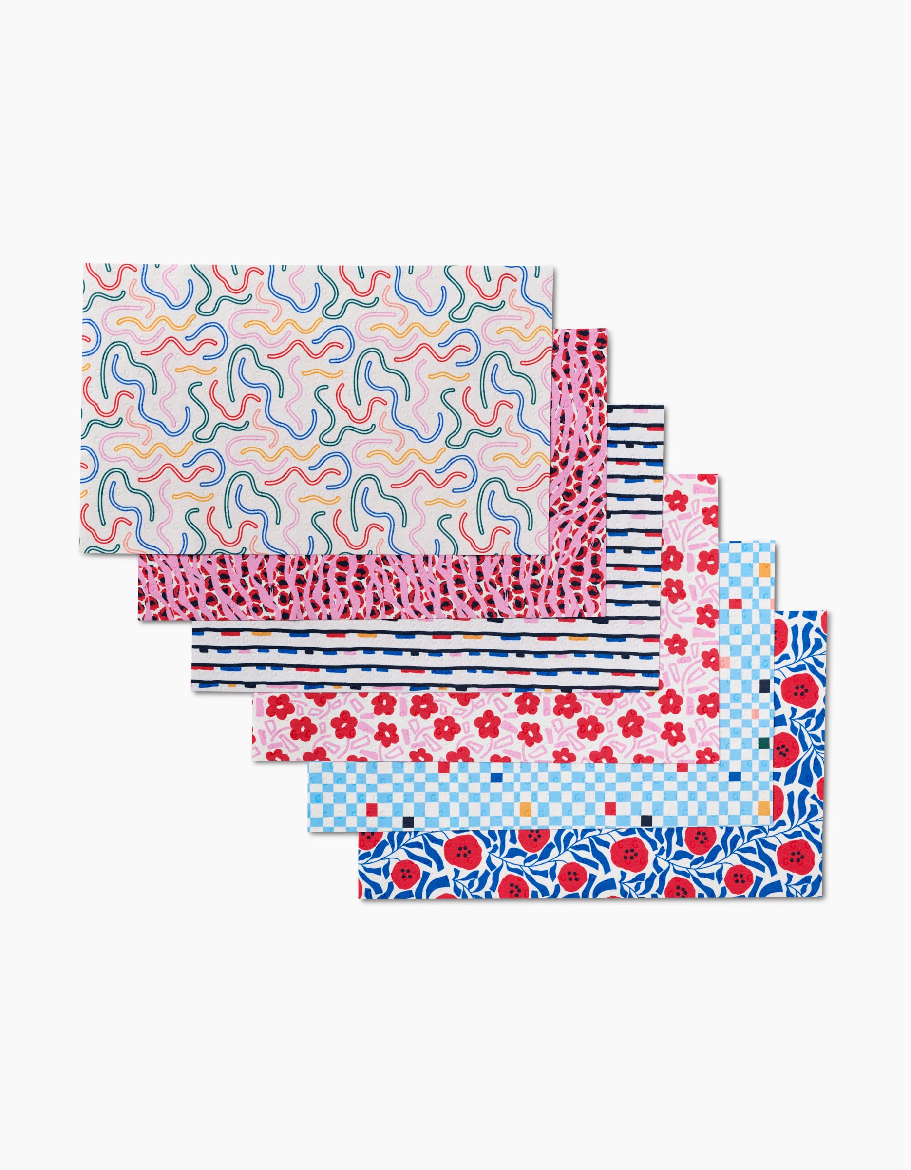 Six Magic Wand sheets by Happy Hemera are stacked, each with a unique colorful pattern—wavy lines, fruit, stripes, floral, and geometric. These eco-friendly towels are made from recycled paper and feature bright designs on white backgrounds.