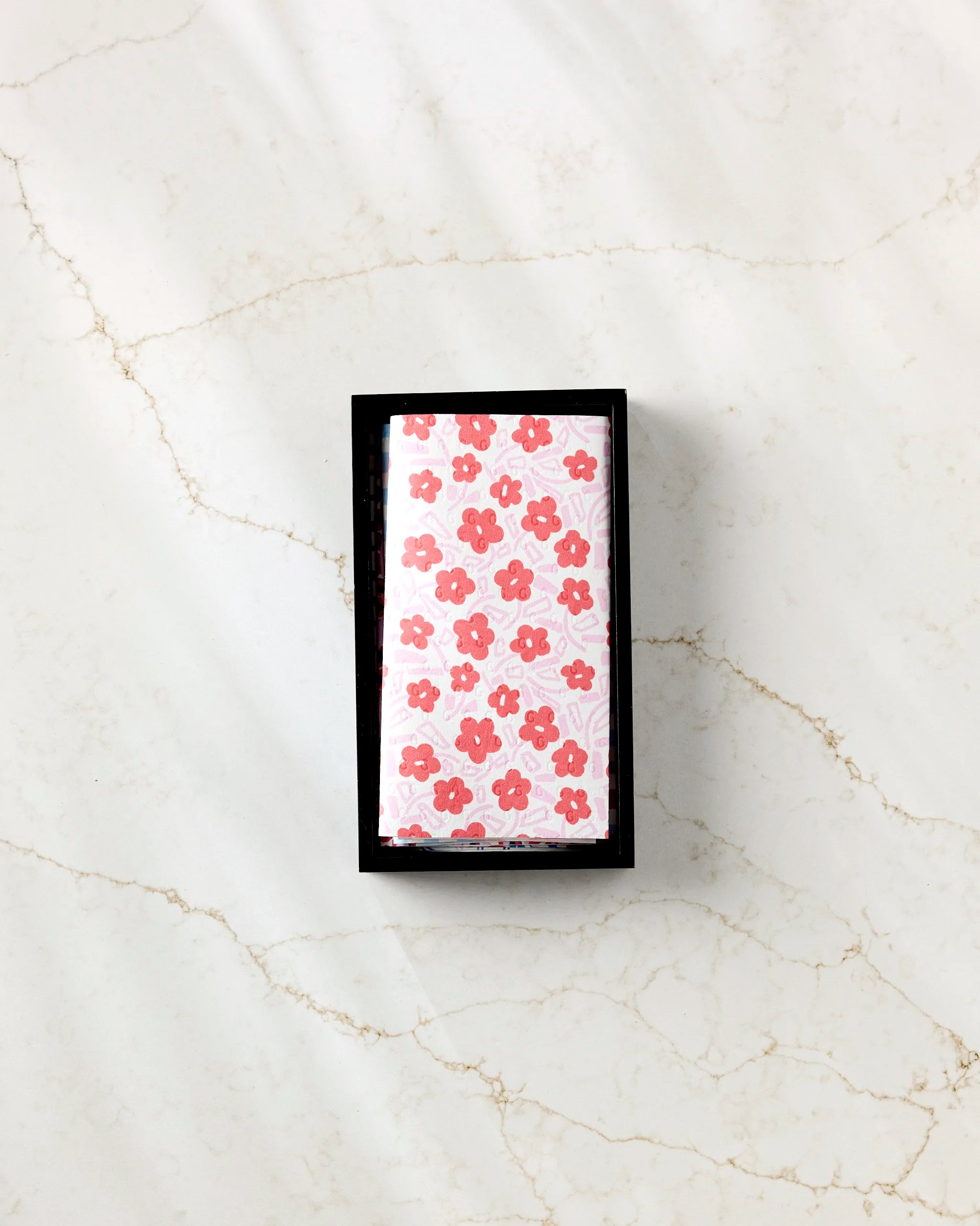 A Magic Wand by Happy Hemera, wrapped in pink floral paper, rests in a black tray on white marble—blending elegance with the eco-conscious appeal of sustainable living.