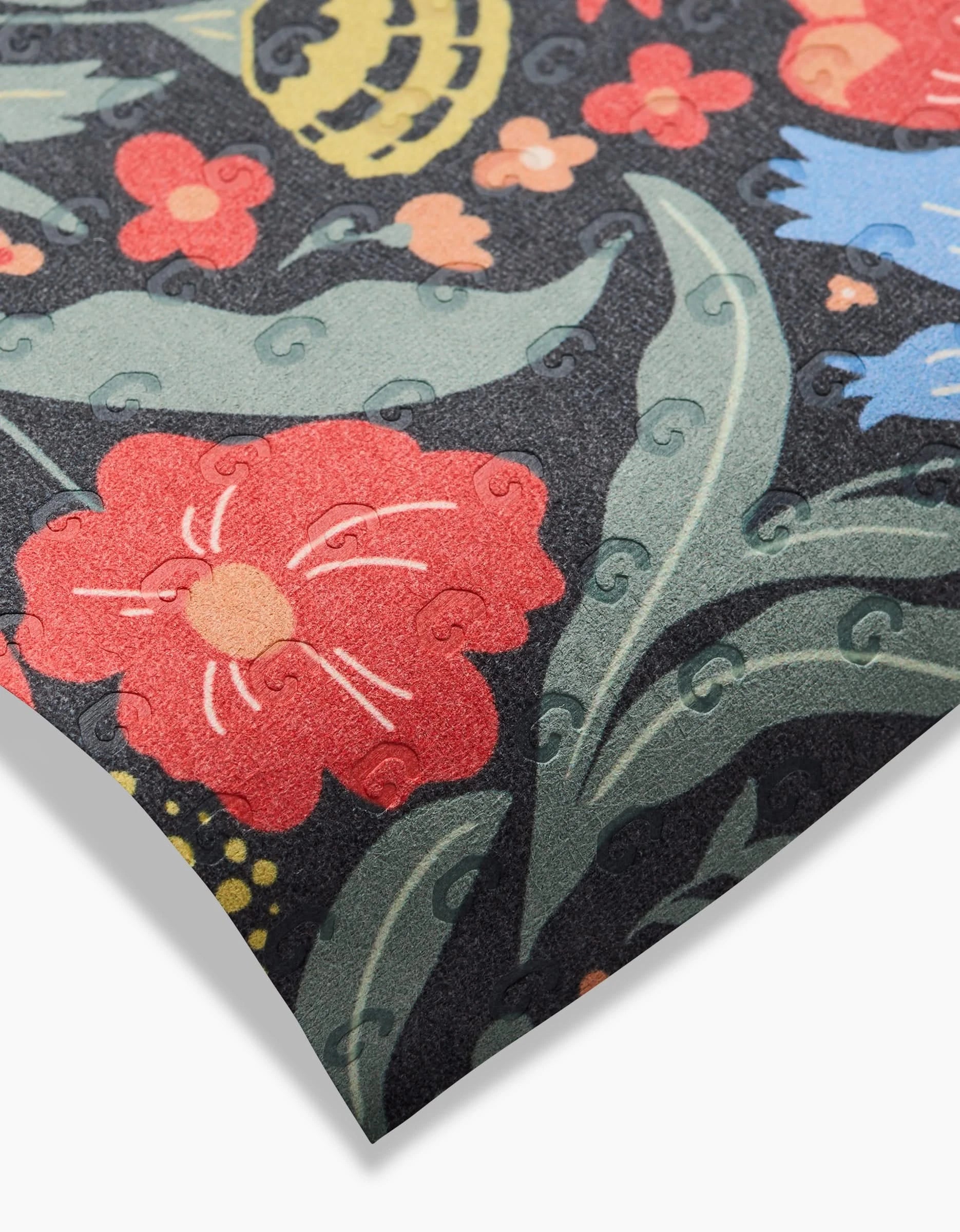 A close-up of the Danelys Sidron Marsh Wren sheet features a colorful floral pattern—red, blue, and yellow flowers with green leaves on dark fabric. The texture and slight embossing are visible. Made from eco-friendly, post-consumer recycled materials.