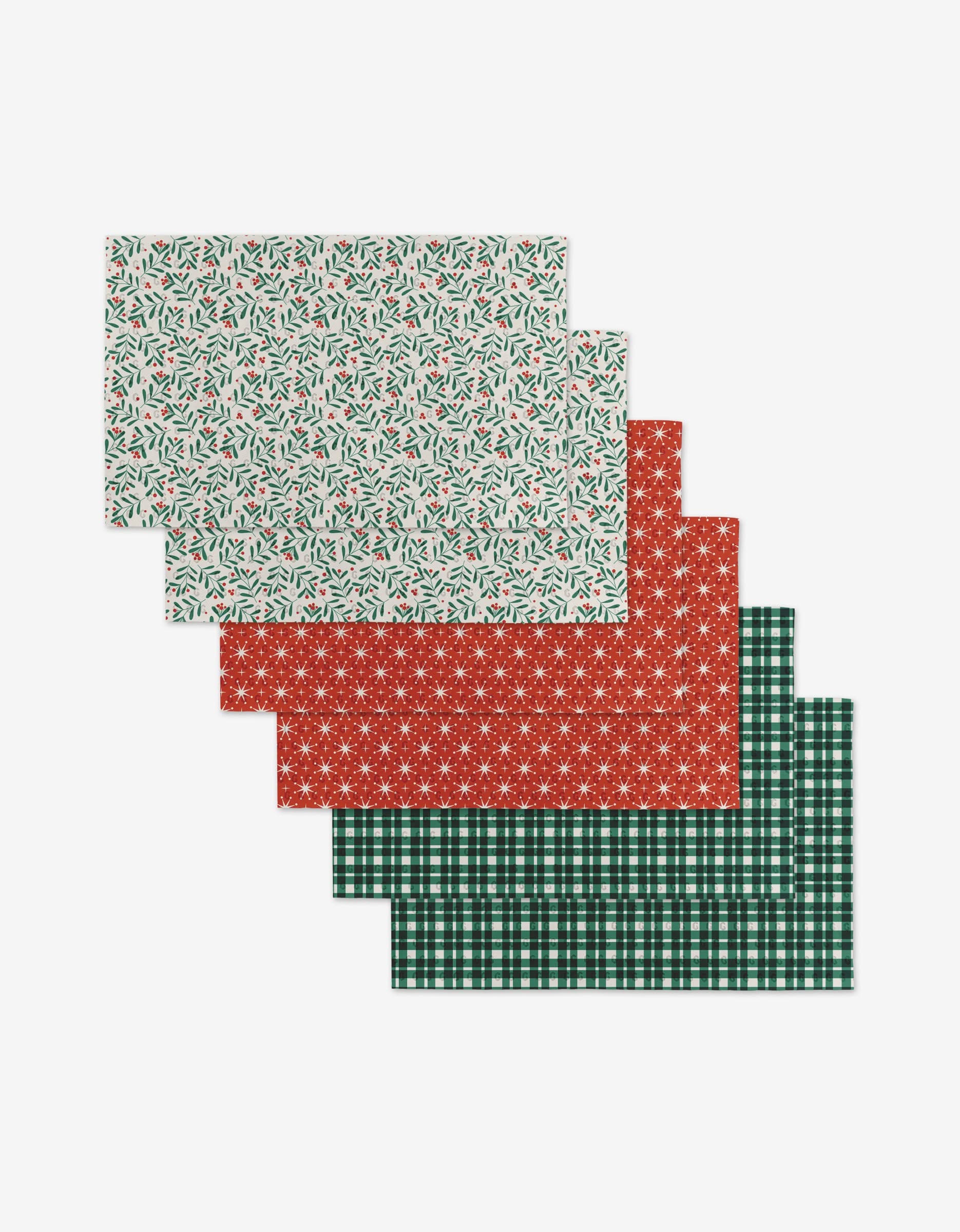 Six Merry Berry placemats by Charlie Rowan Designs, featuring holly leaves with berries on white, red snowflakes, and green plaid patterns, are fanned out on a white background. Made from eco-friendly post-consumer recycled materials.