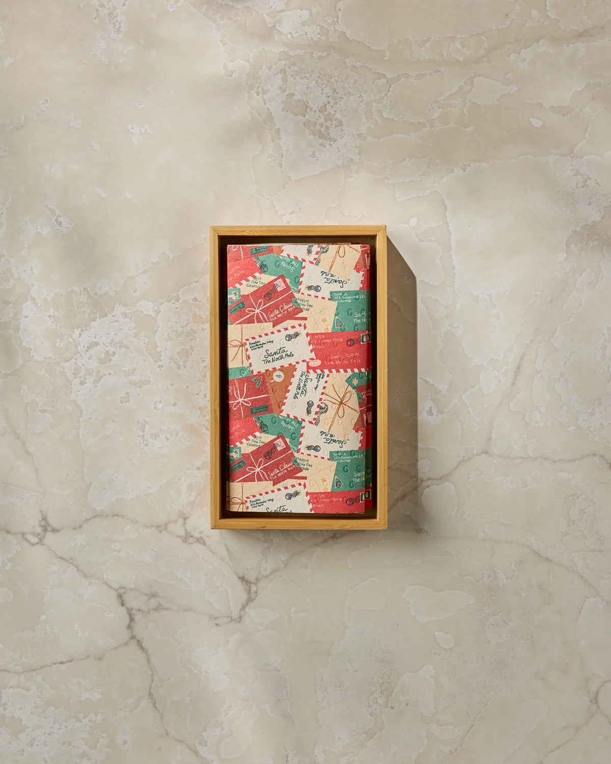 The “Merry Mail” by Geometry is a rectangular wooden box featuring a bar wrapped in festive red, green, and gold paper adorned with holiday designs—an eco-friendly detail ideal for the season. Presented on a light marble surface, this set pairs elegantly with Geometry’s reusable paper towels, offering a sustainable alternative to disposables for your home.