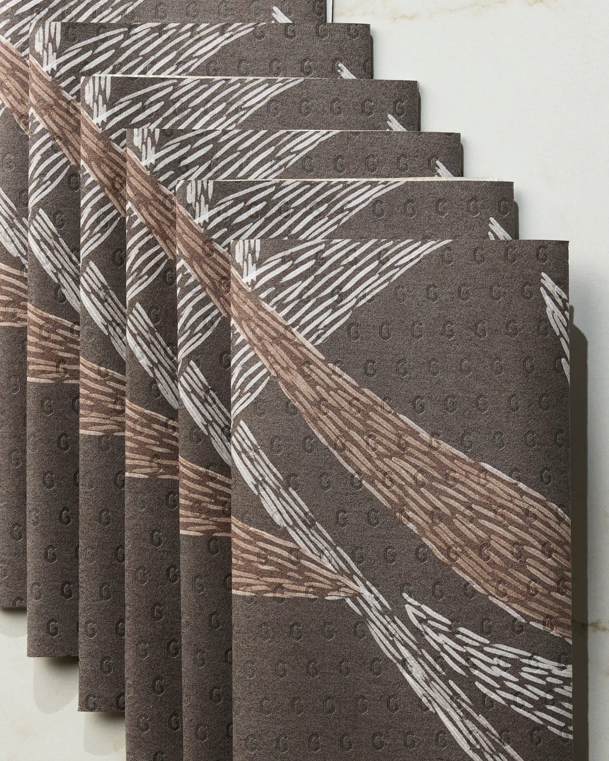 Geometry’s Midnight Wildflower reusable paper towels, featuring a textured pattern with white and brown diagonal brushstroke designs, are shown neatly stacked on a light marble surface.