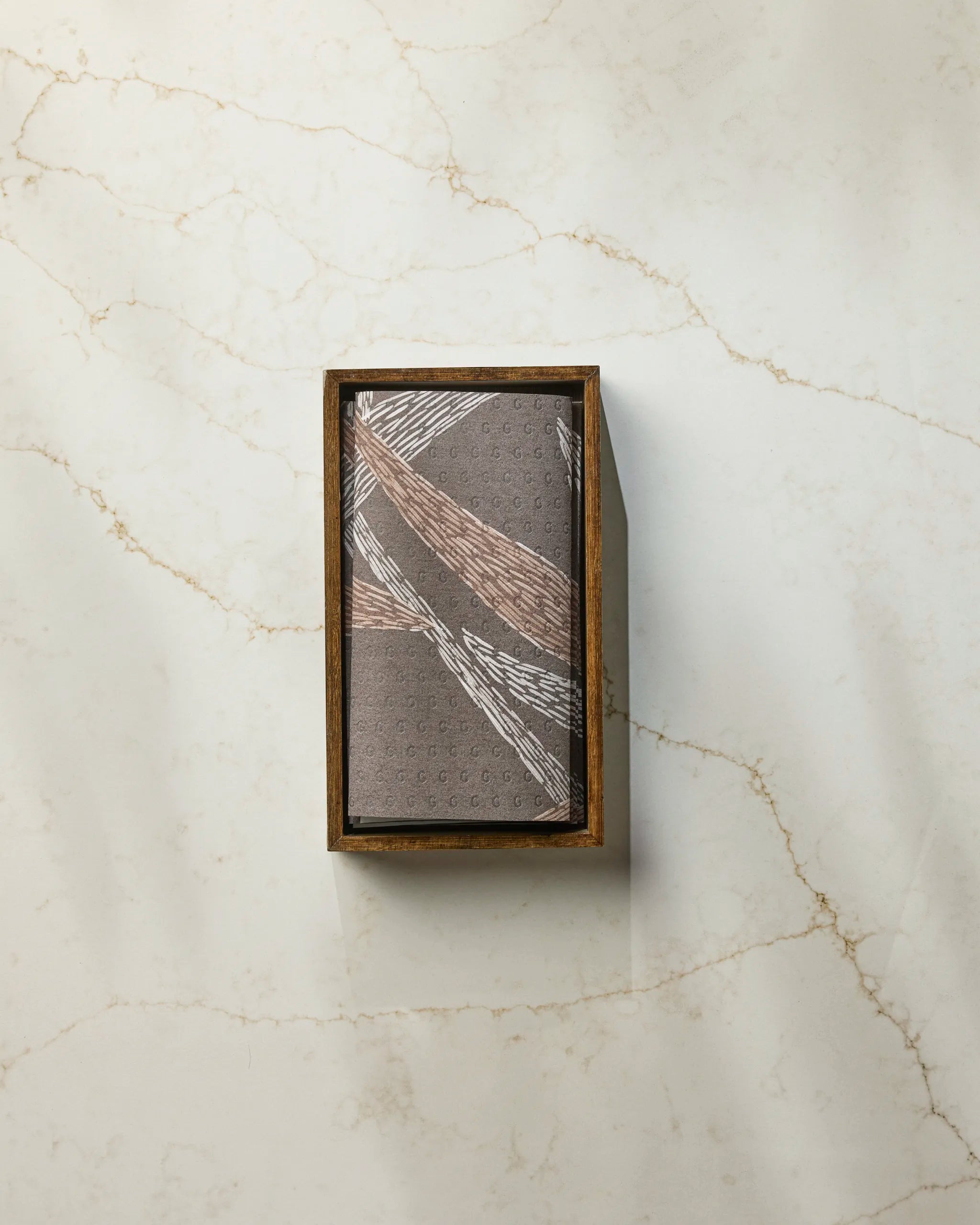 The Geometry Midnight Wildflower rectangular wooden box features a patterned lid with intersecting metallic lines and sits on white marble with light brown veining, ideal for storing eco-friendly paper towels.