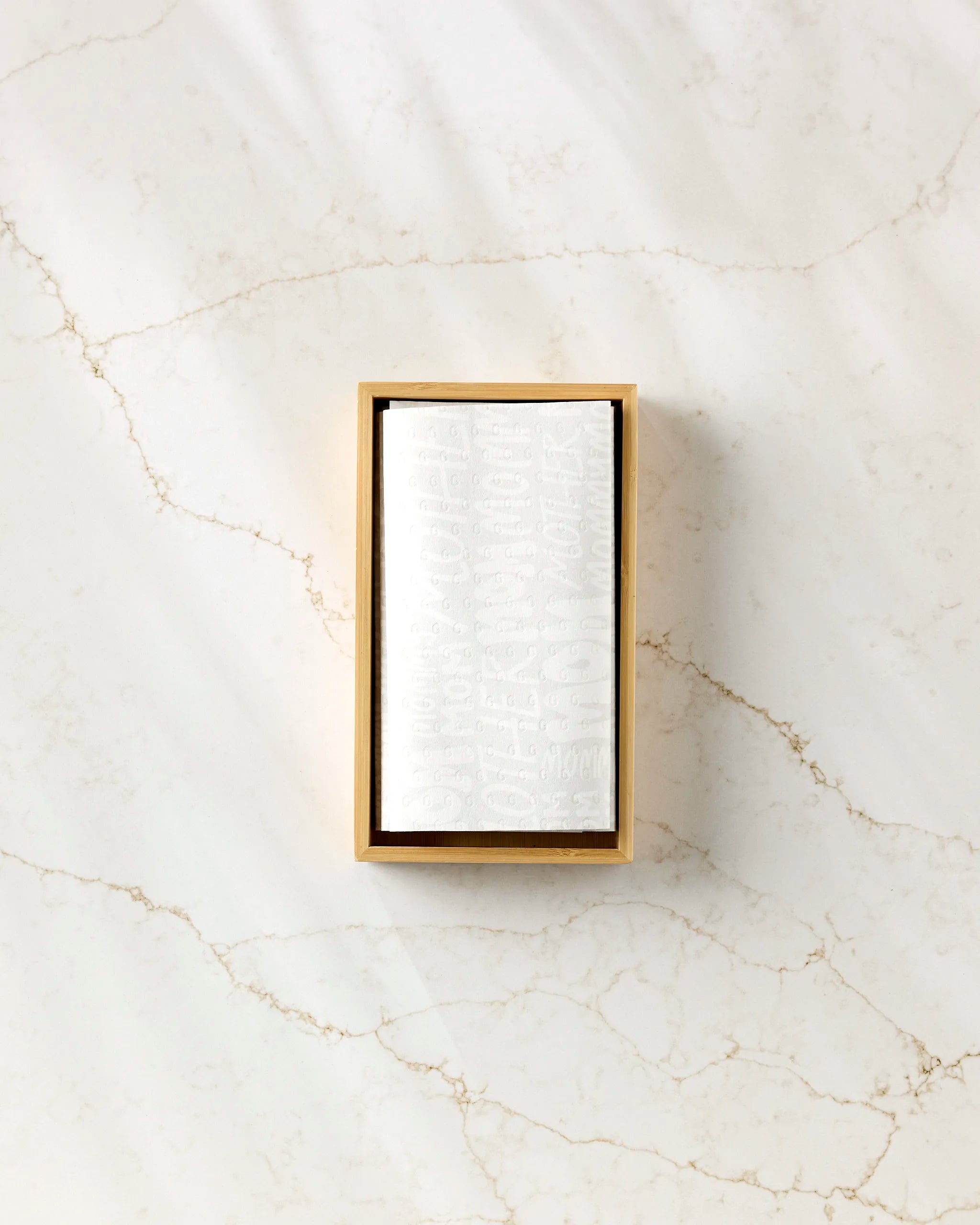 A rectangular wooden box with a white card featuring subtle embossed text, placed on a light marble surface with soft natural lighting—perfect for displaying GEOMETRY’s eco-friendly Mom kitchen towels or reusable paper towels.