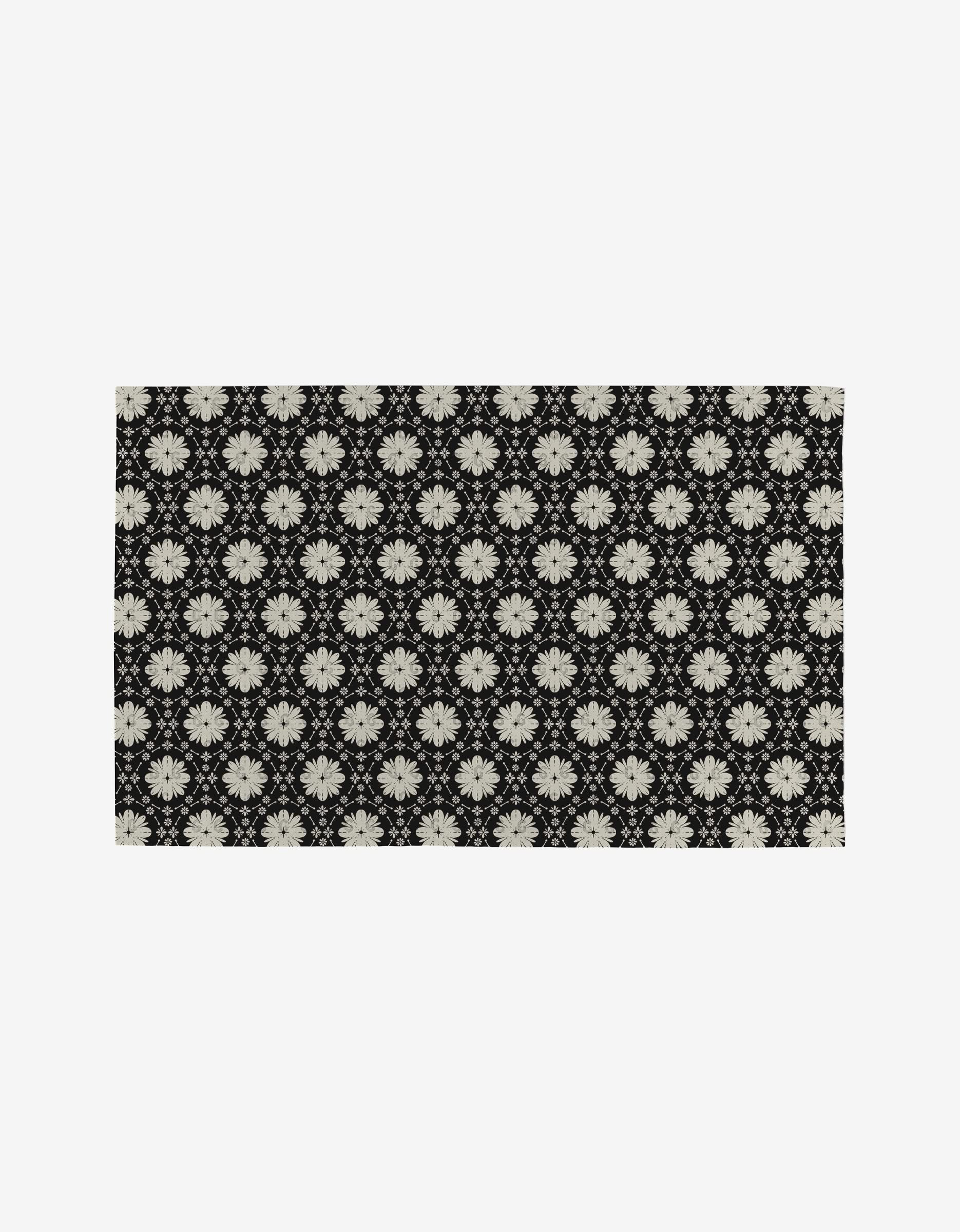 The Monochrome Florals rug by Danelys Sidron features a black background with white floral patterns in a grid, crafted from post-consumer recycled materials for an eco-friendly choice.