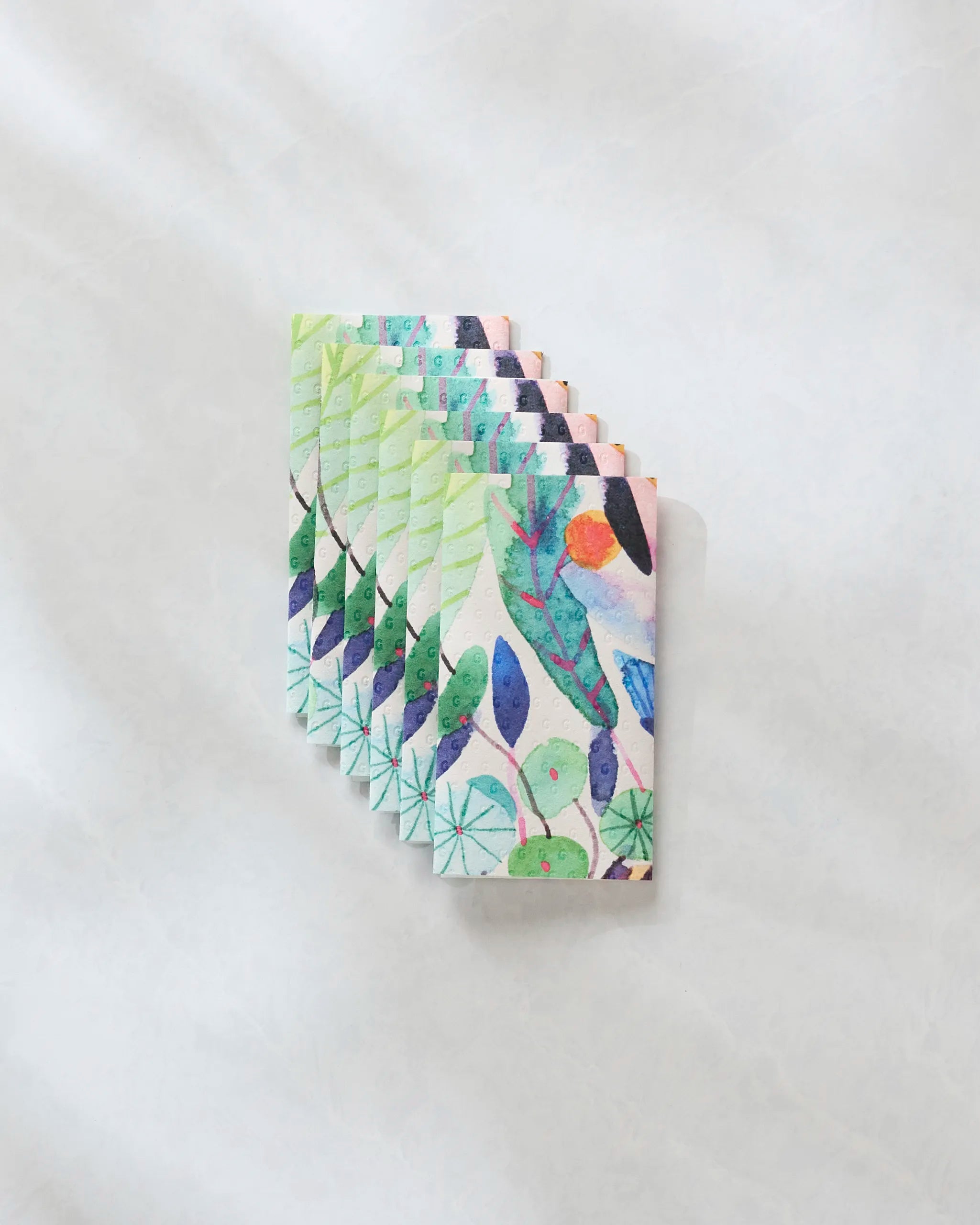 Eight illustrated cards from Maria Montiel's "Morning" collection, featuring vibrant abstract leaf and plant designs, are elegantly fanned out on a light, textured surface, blending sustainability and style for everyday living.
