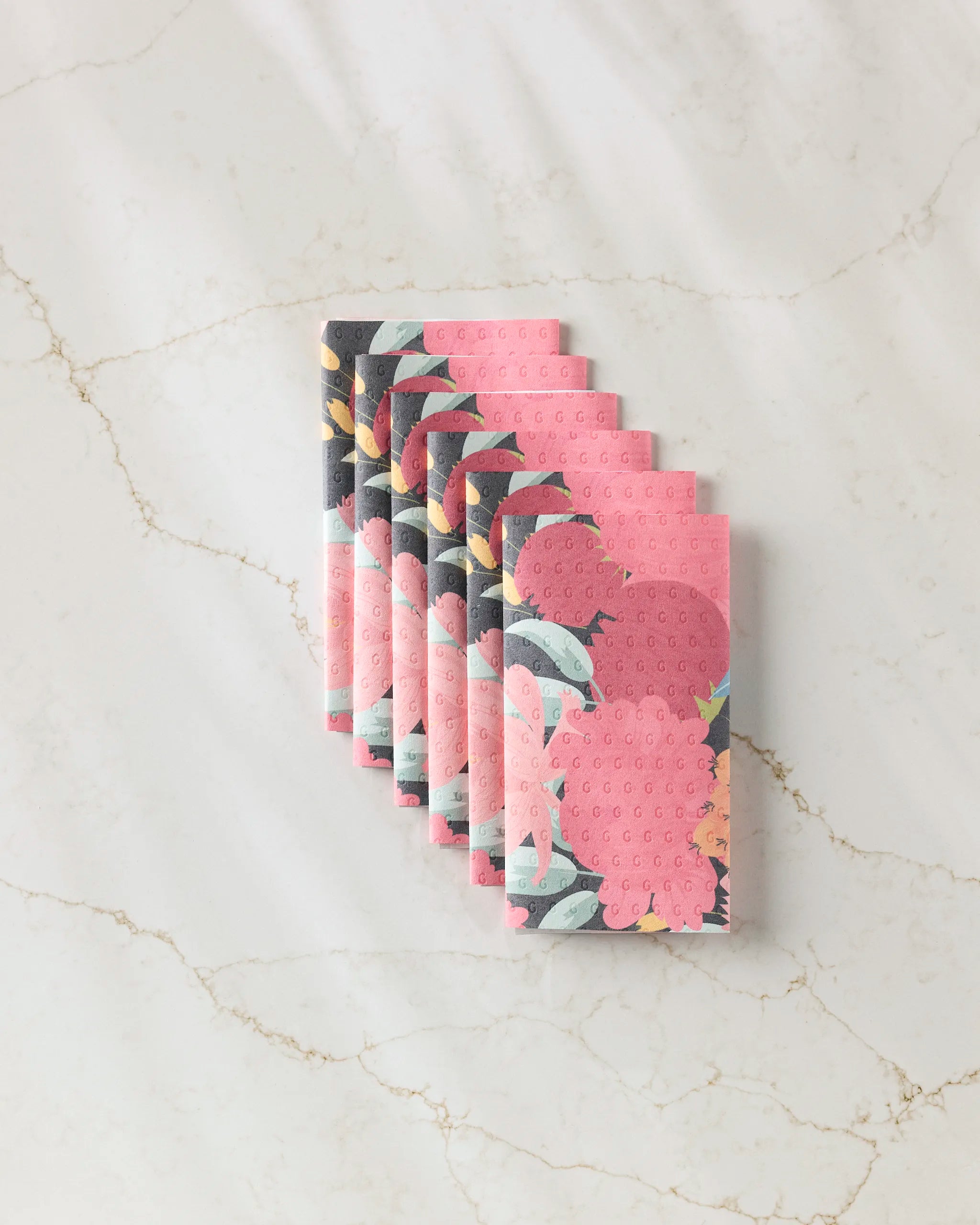 Eight "My Garden" sponge cloths by GEOMETRY, featuring a pink floral design and made from eco-friendly paper towels, are neatly fanned out on a white marble surface.