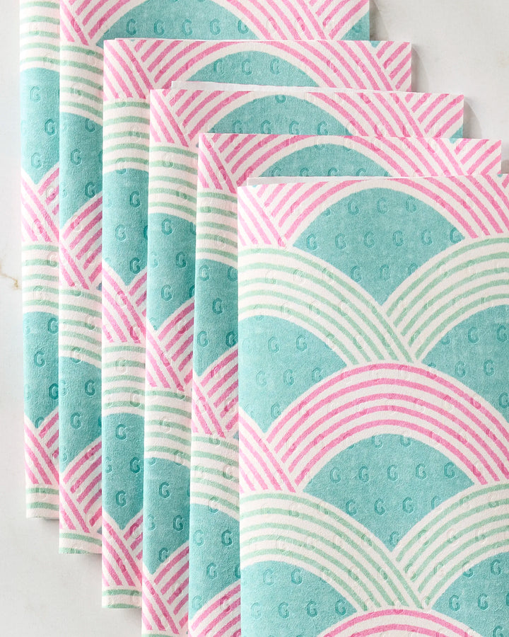 Five eco-friendly Nalin paper towels by Amy MacCready, featuring a retro geometric pattern of teal, pink, and white scallops and lines, are neatly stacked on a light surface.