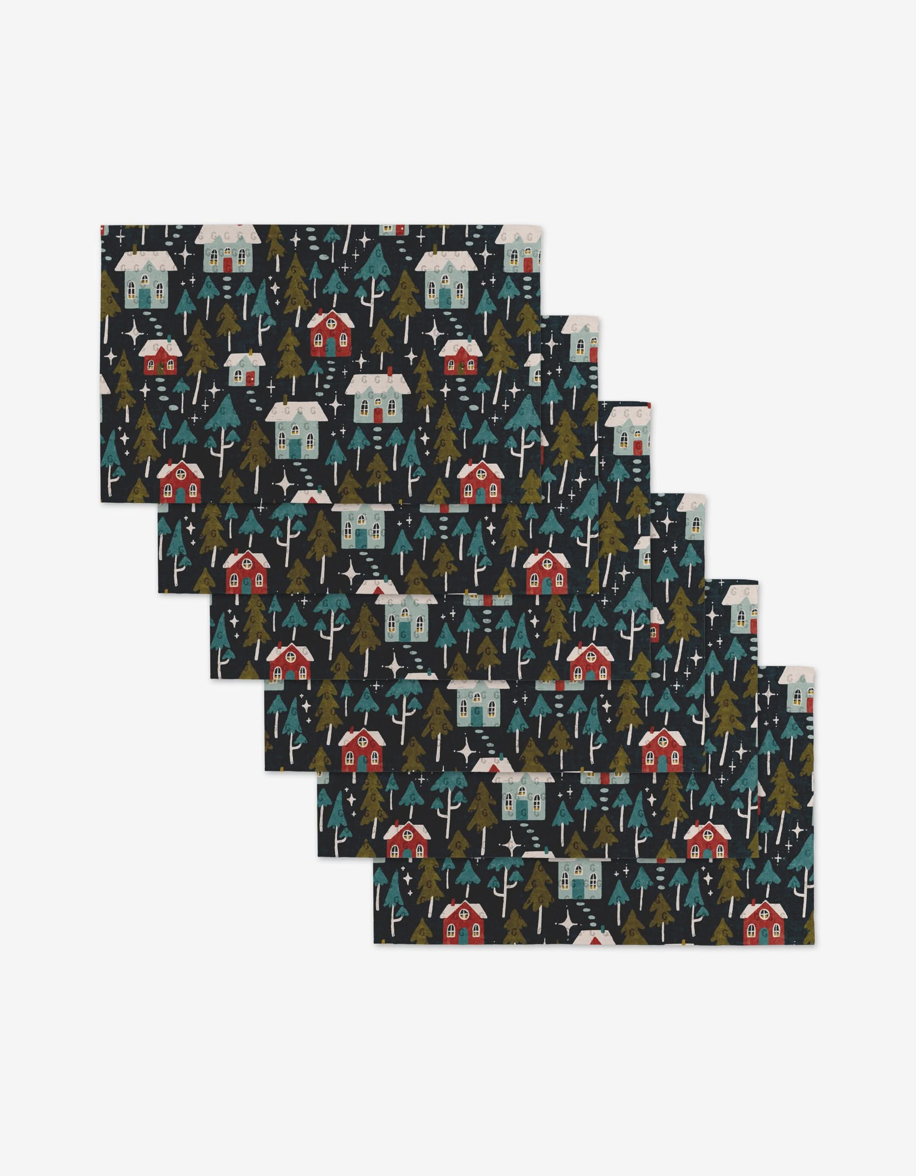 Six Nico Dark placemats by Amy MacCready, stacked and showcasing a winter village scene of houses, trees, and snowflakes on a dark background—ideal for an eco-friendly table setting with reusable towels.