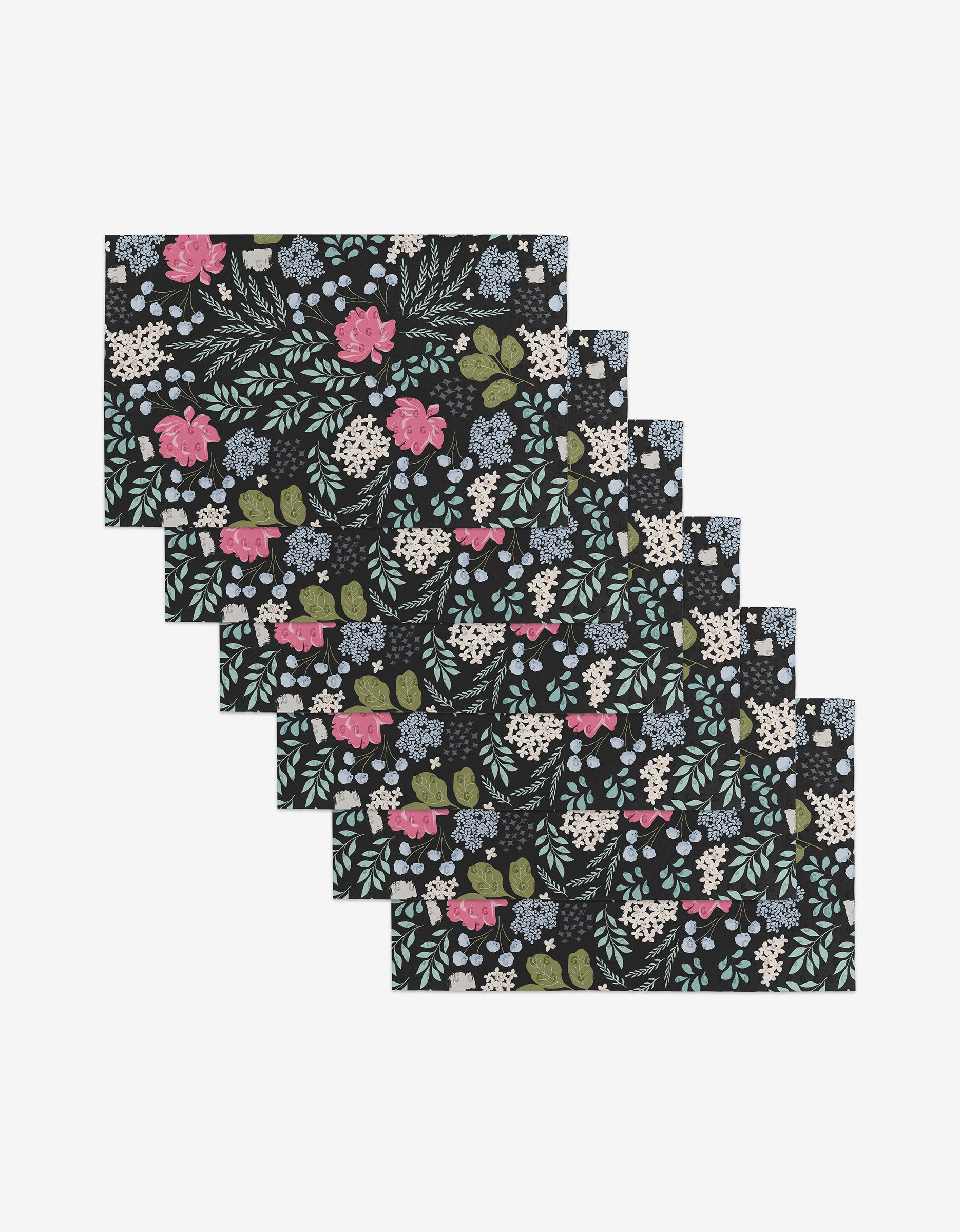 Six Not Forgotten rectangular placemats by GEOMETRY: black background with a floral pattern in pink, blue, white, and green—crafted from post-consumer recycled materials—shown overlapped in a stack.