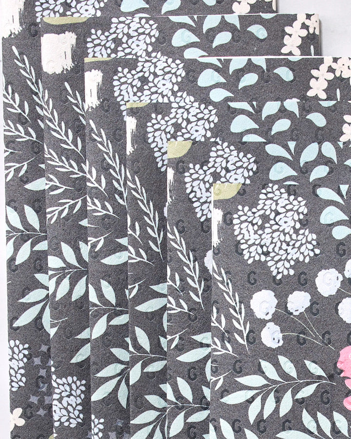 Not Forgotten by GEOMETRY features several dark, reusable paper towels with a repeating floral pattern in light blue, teal, white, pink, and yellow arranged in a fanned-out display.