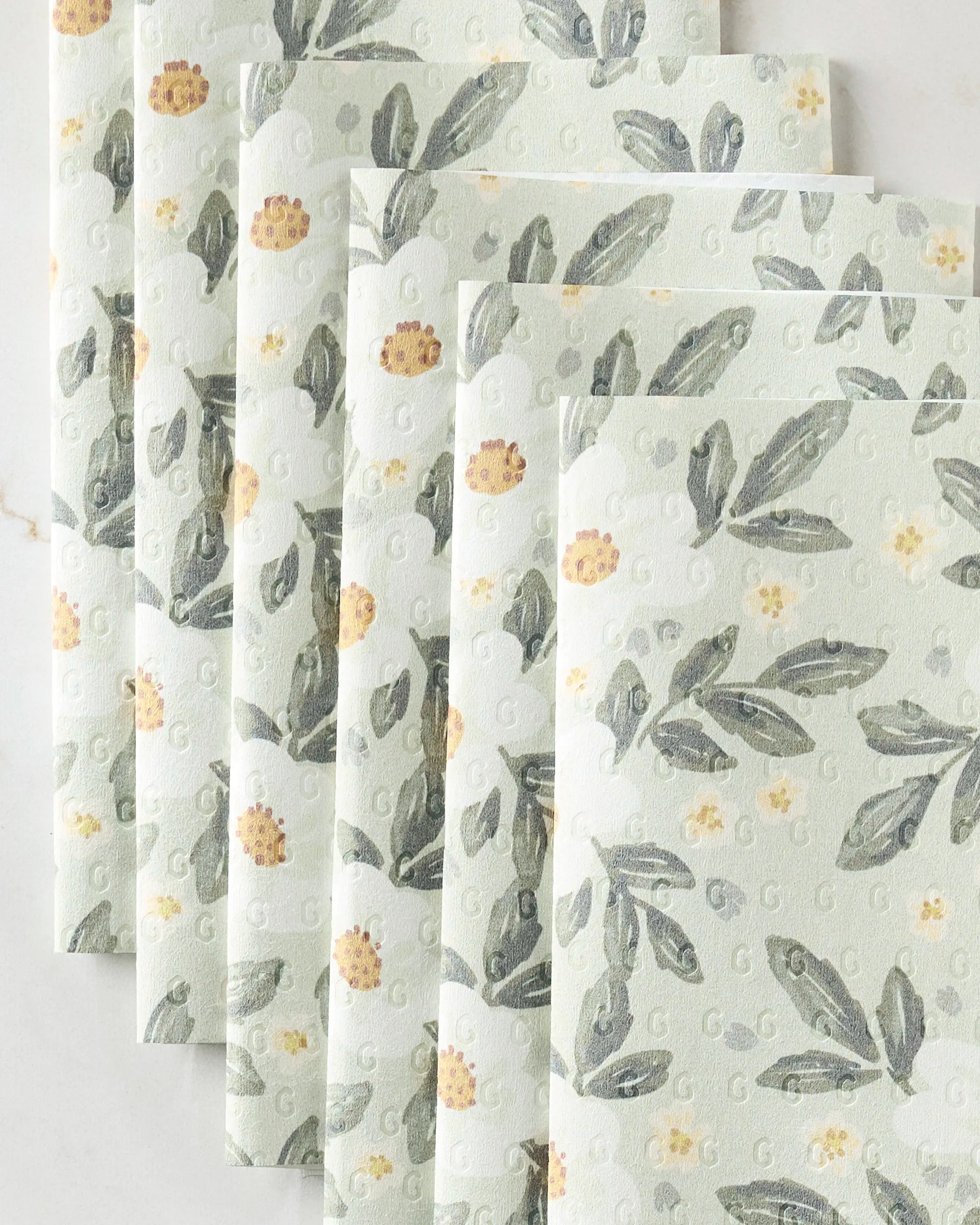 Teri the Butter's Painted Spring Flowers paper towels, eco-friendly in light green with a floral pattern of yellow flowers and green leaves, are fanned out on a white surface.