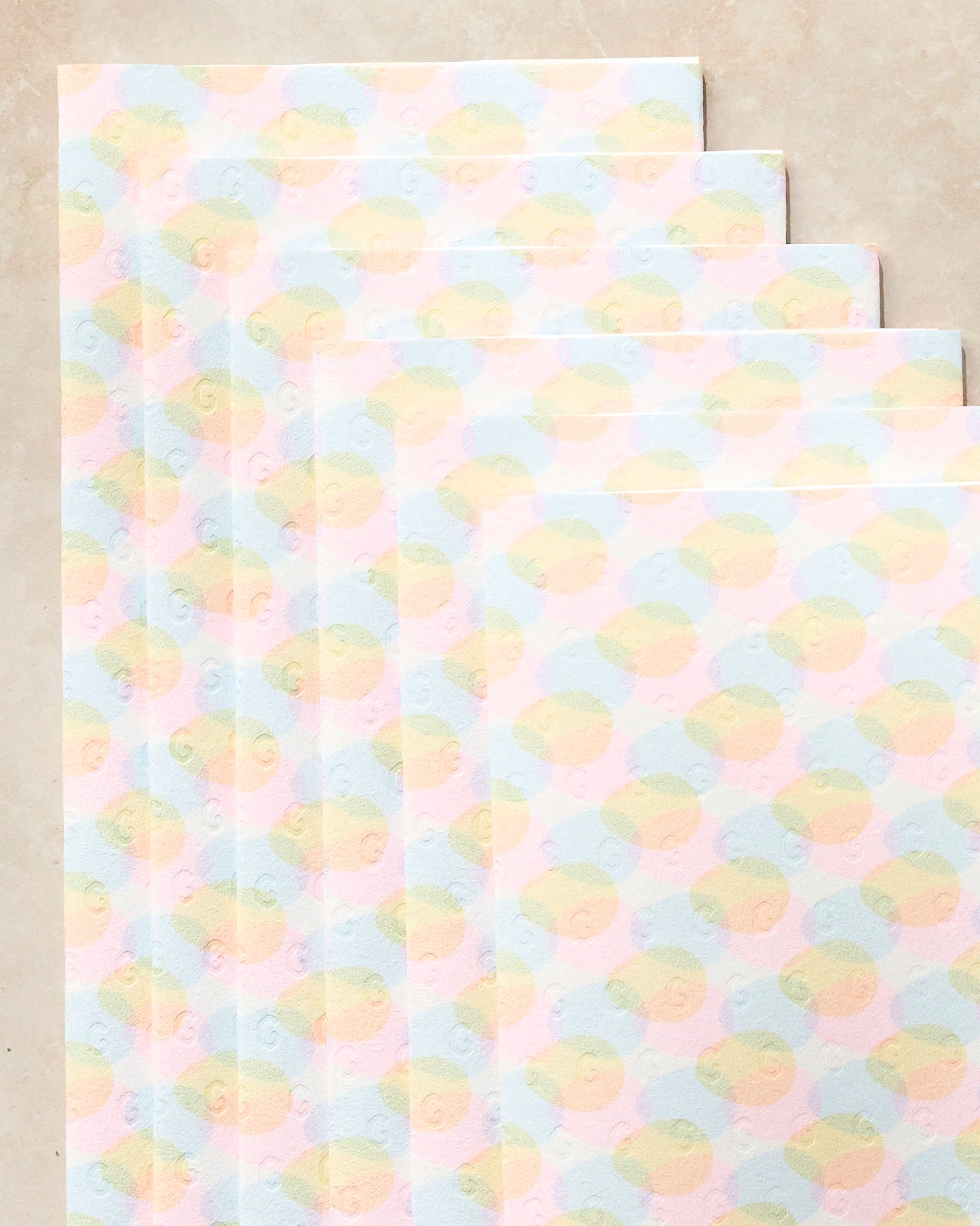 Six eco-friendly Geometry Pastel Pop kitchen towels are fanned out on a light beige surface, each sheet displaying a repeating pattern of soft pastel circles.