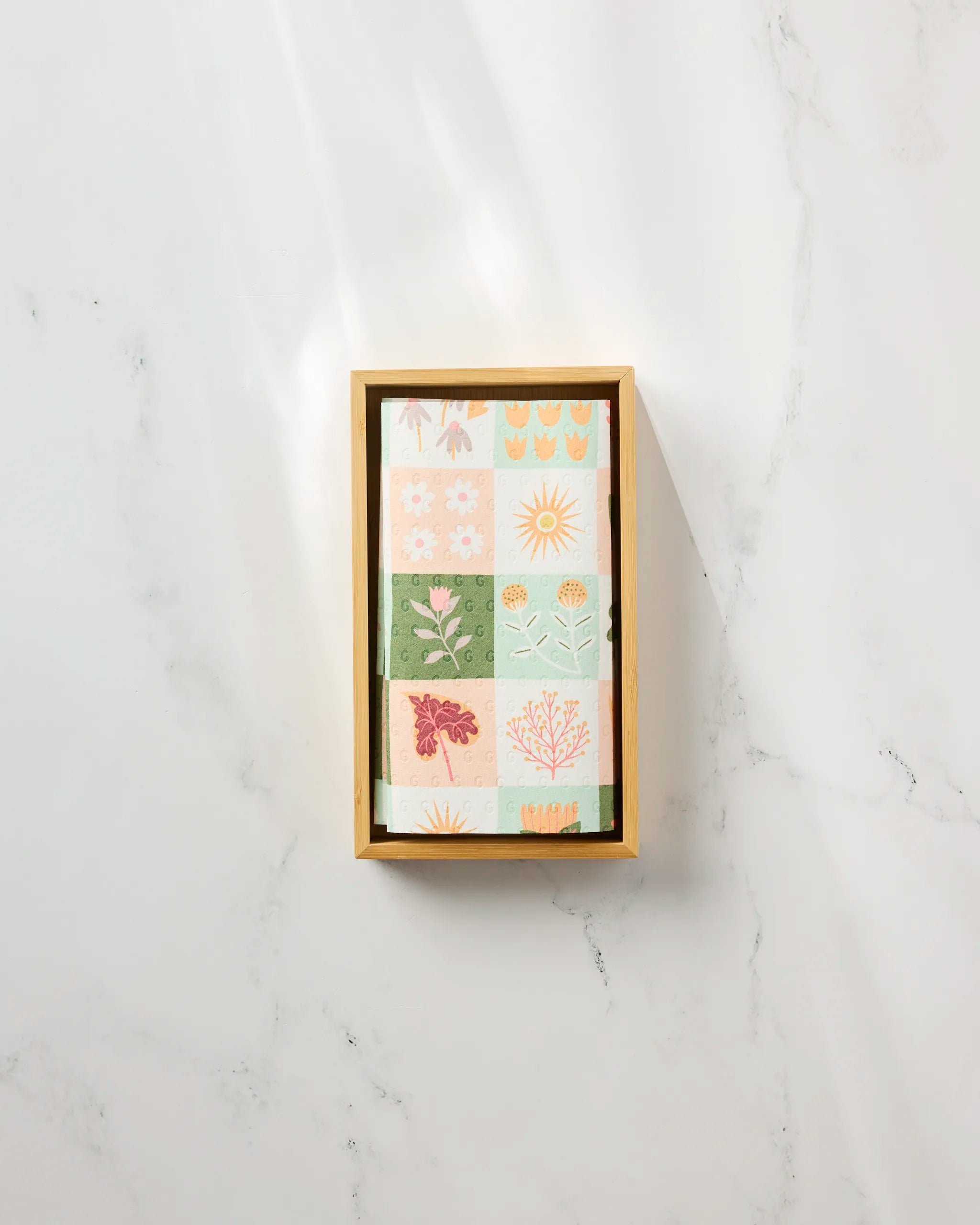 The Patchwork Garden tray by Rachel Parker displays pastel, reusable paper towels with floral and sun-themed patterns, all arranged on a light marble surface.