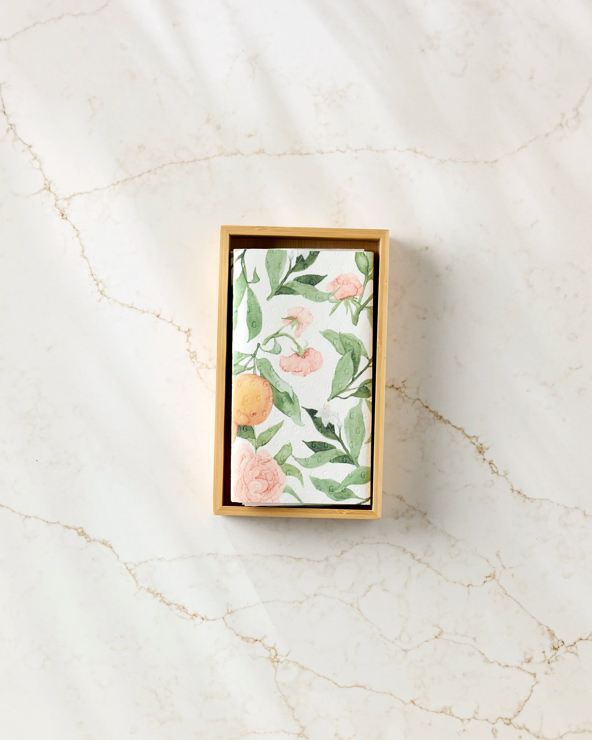 Aubrey Fairchild’s “Peony For Your Thoughts” features a rectangular box with a floral and citrus card inside, set on veined marble—an elegant way to present eco-friendly kitchen towels.