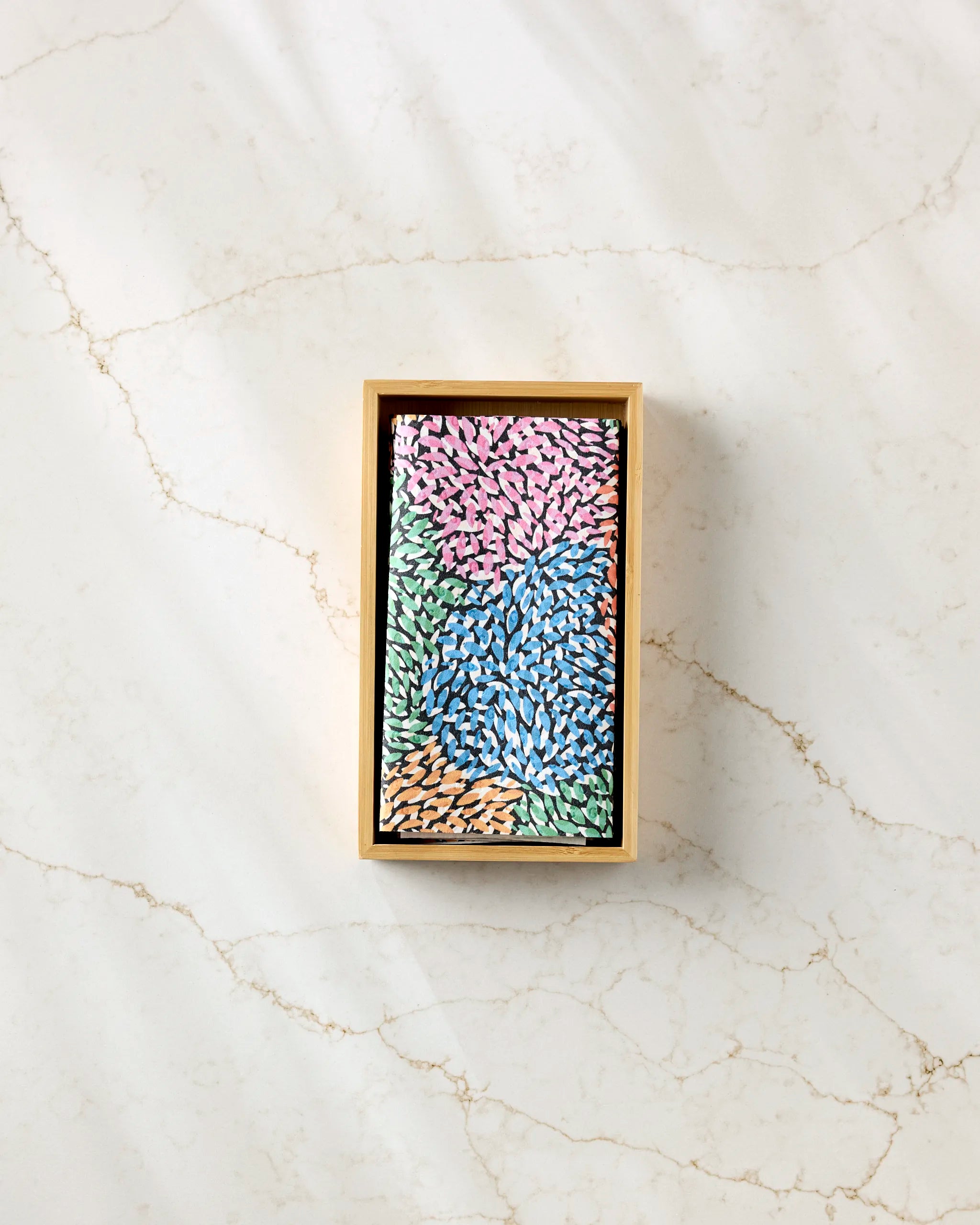 A rectangular box of Rachel Parker's Petal Pen sits on a light marble surface, its packaging adorned with colorful petal-like patterns in pink, blue, green, and tan—a stylish addition to any eco-friendly workspace.