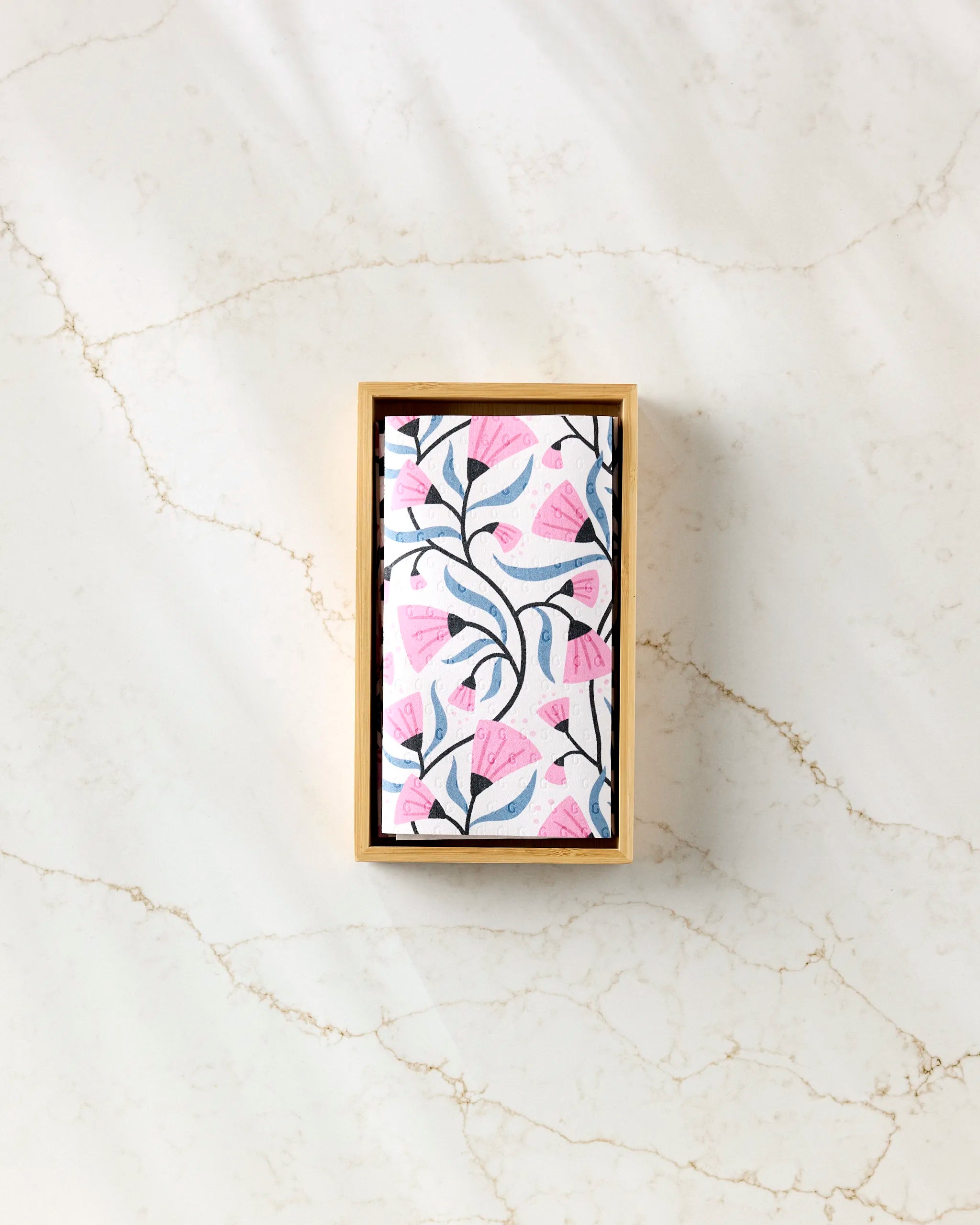 The Petal Symphony note cards by Anette Heiberg feature a pink and gray floral design in a rectangular wooden box, displayed on white marble next to neatly folded eco-friendly kitchen towels.