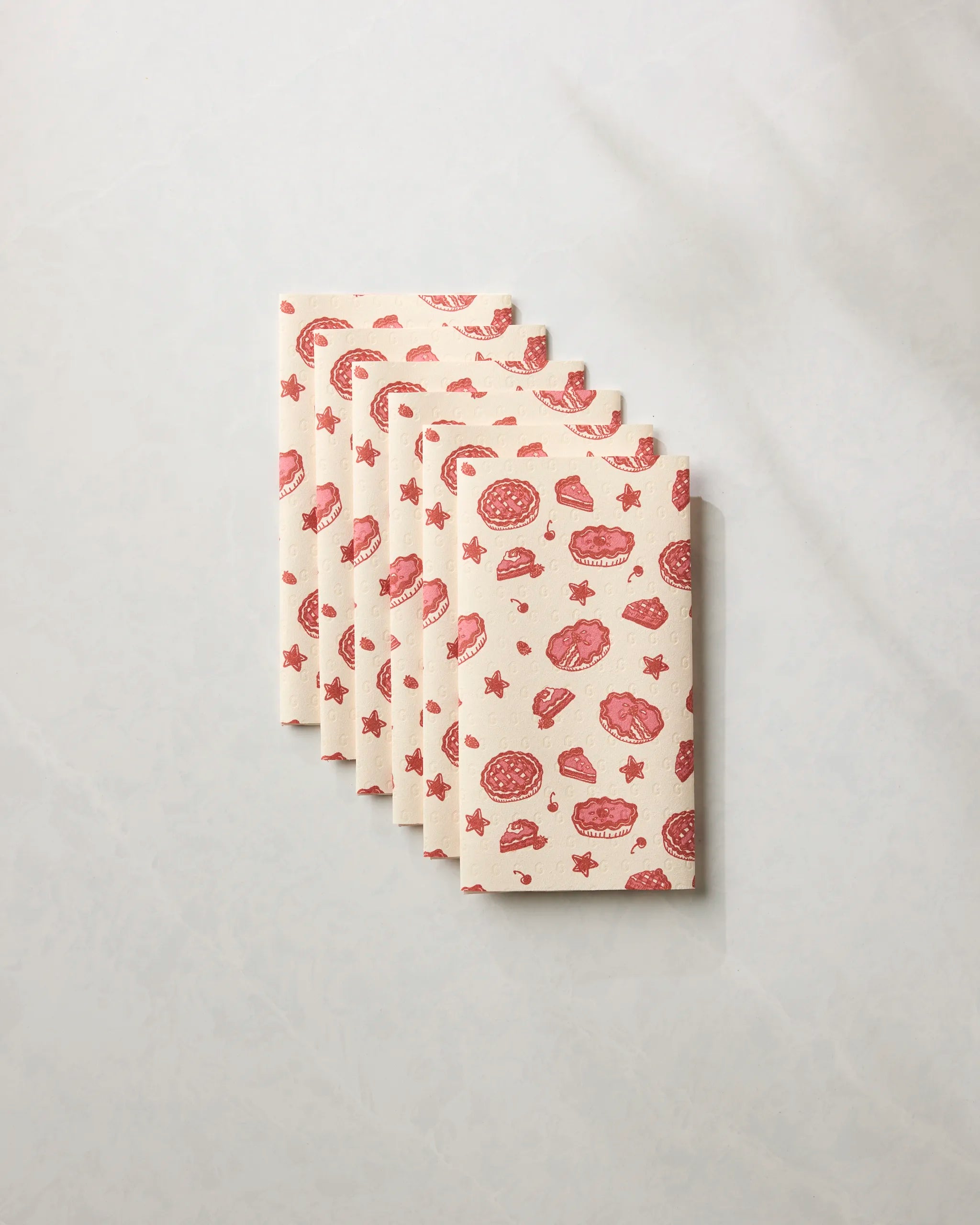Six Geometry Pie-triotic cloth napkins with a pink and red bagel, doughnut, and star pattern on light beige—an eco-friendly reusable paper towel alternative for your table, shown fanned out in a stack.