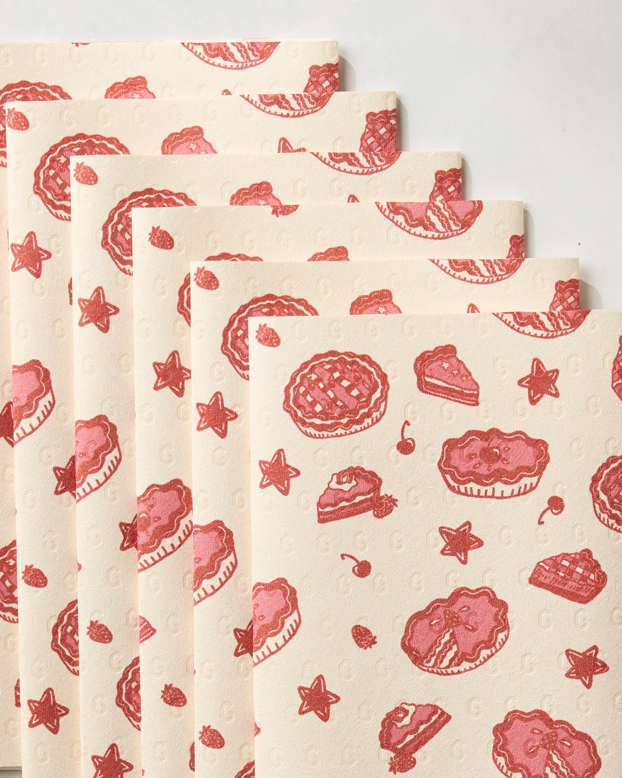 The Geometry Pie-triotic set features seven cream-colored reusable paper towels, each with red pie, cherry, and star prints on a light background arranged in a fanned-out display.