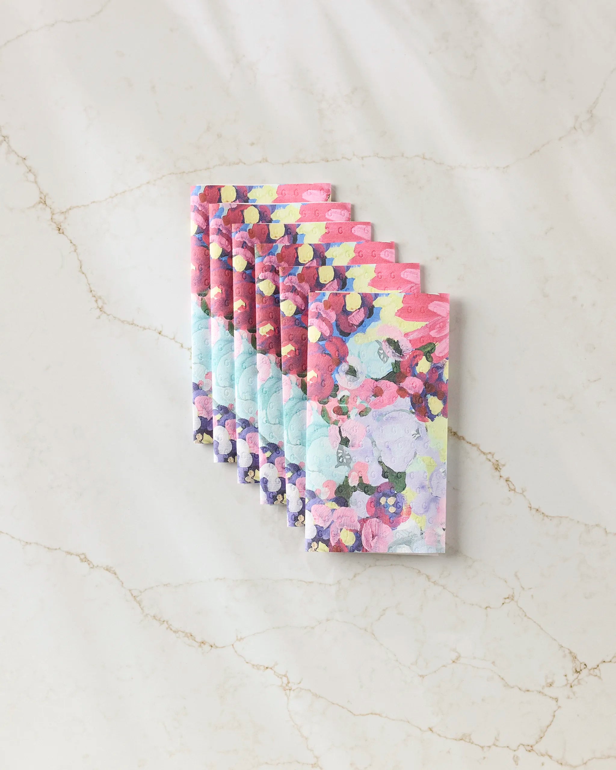 The "Pink Fields of Joy" notebook set by Ania Zwara Art features six vibrant, abstract-covered notebooks made from eco-friendly paper towels, beautifully fanned out on a light marble background.