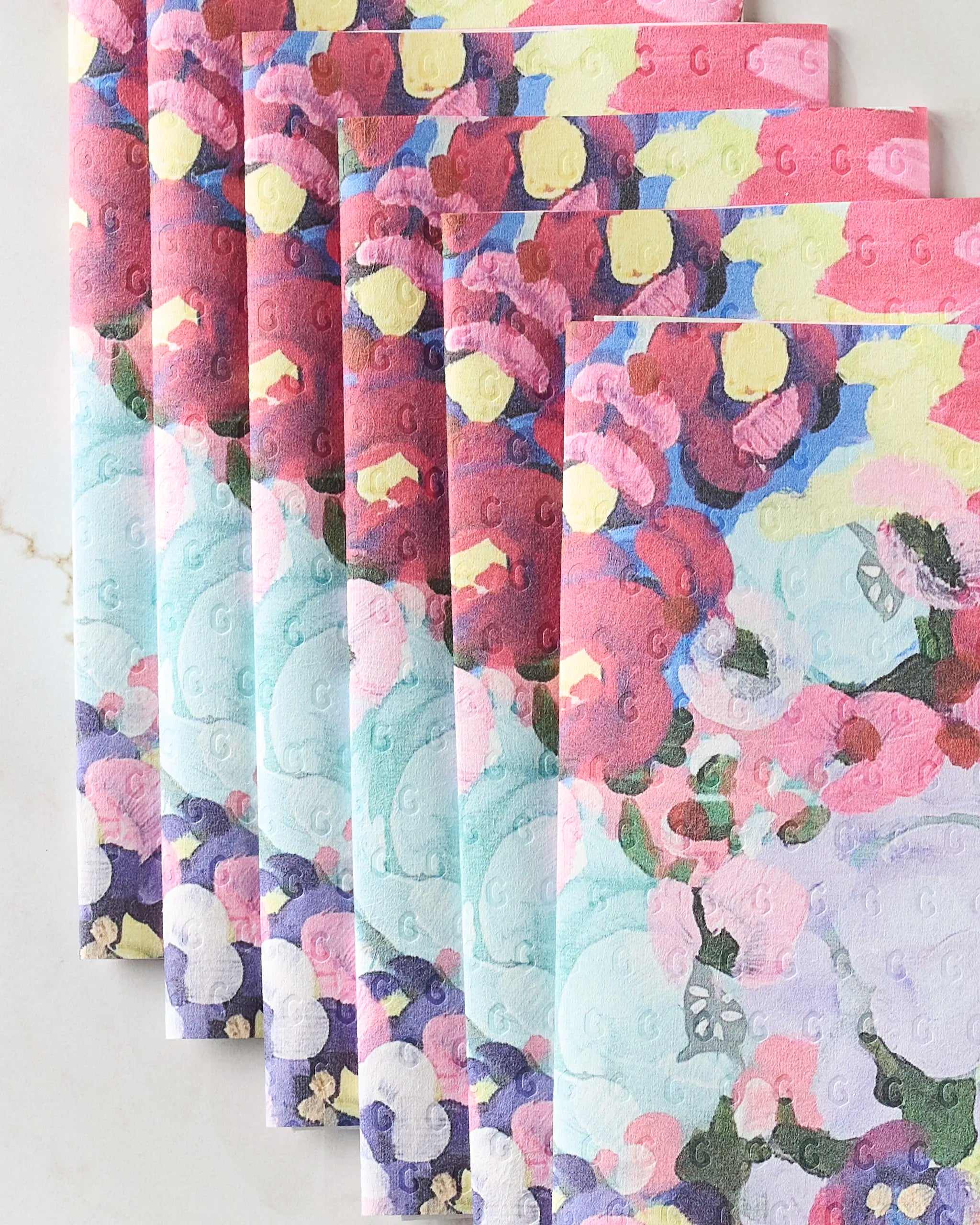 Seven folded Pink Fields of Joy paper towels by Ania Zwara Art are arranged in a fan shape, displaying vibrant abstract floral patterns in pink, red, yellow, blue, and purple on a white background.
