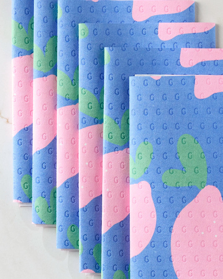 A set of Pink Lemons reusable paper towels by Jennifer Bouron, featuring blue, pink, and green patterns with a subtle repeating G texture, is neatly stacked in a fanned arrangement on a light surface.