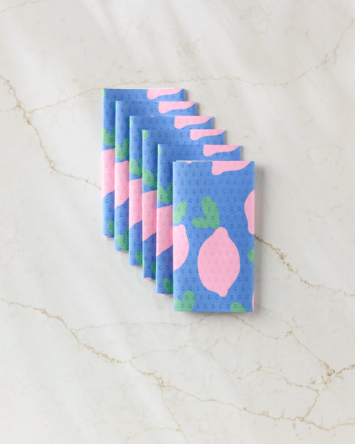 Seven Pink Lemons reusable paper towels by Jennifer Bouron, featuring a pink and green lemon pattern on blue, are arranged in a neat, overlapping row on a marble surface.