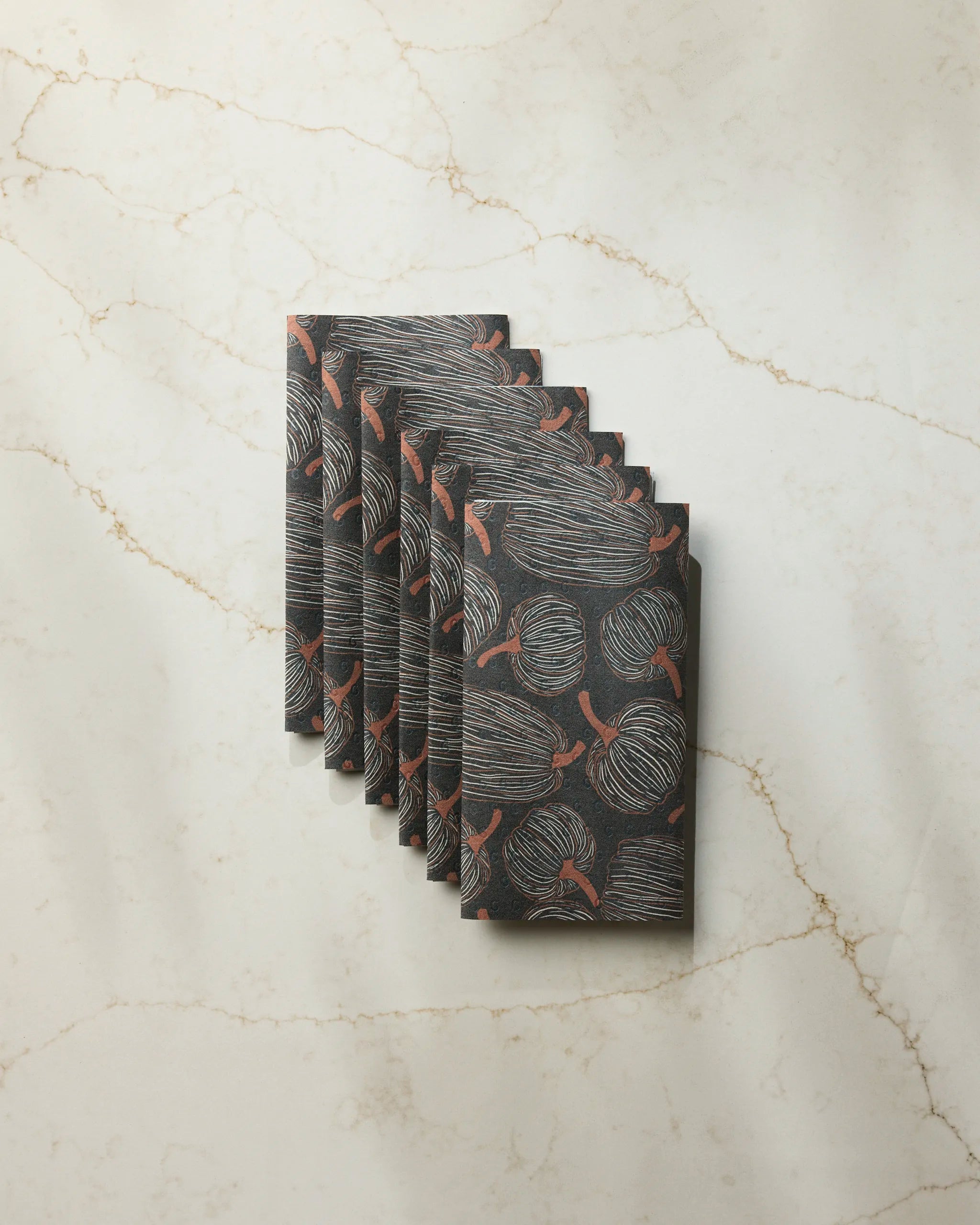 Six folded black napkins in the "Pinstripe Patch" pattern by Geometry, arranged on light marble—an elegant, eco-friendly paper towel alternative for your table.