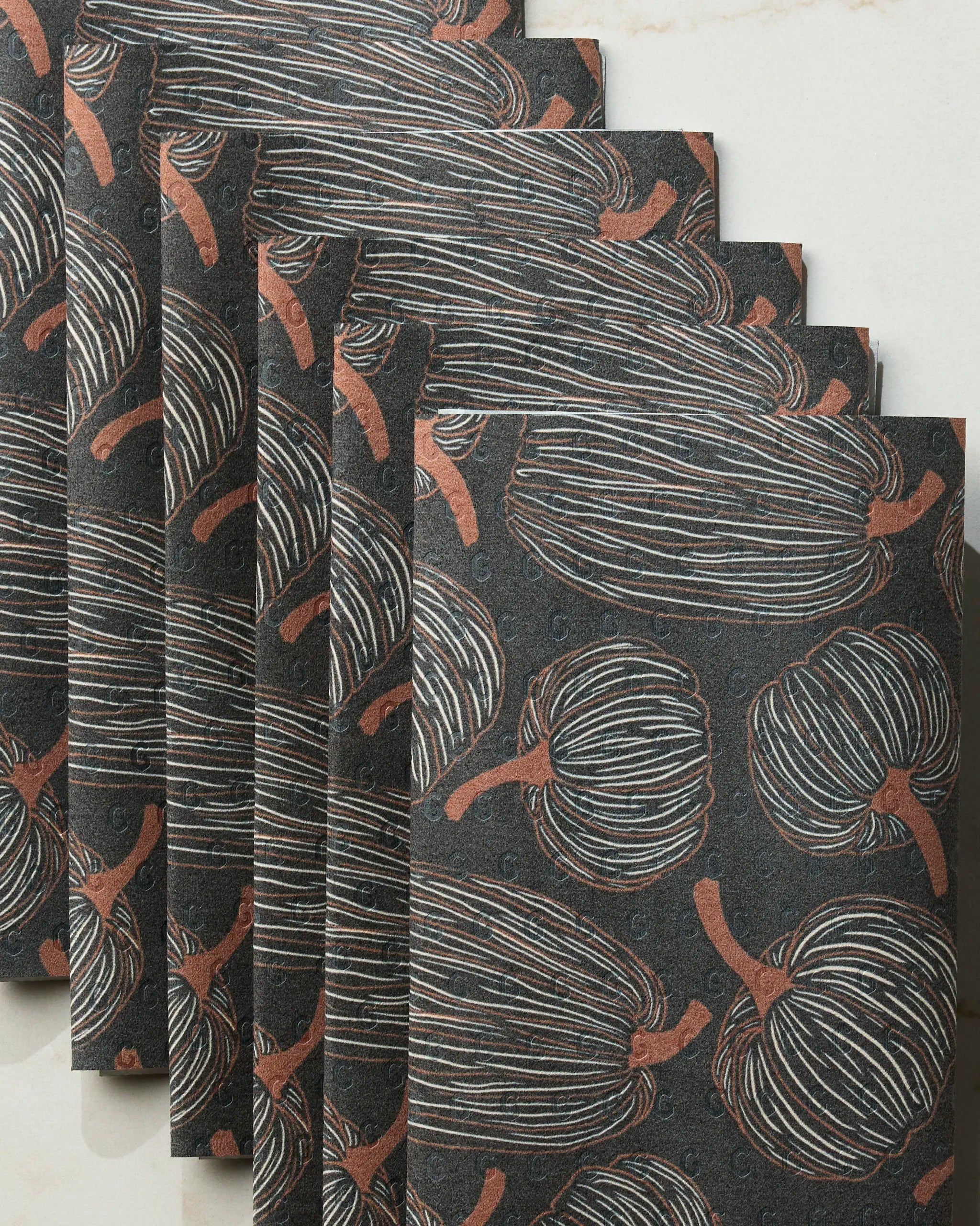 Six Pinstripe Patch napkins by Geometry, featuring a thin white and copper pumpkin pattern on black, are stacked on a light surface—an eco-friendly and elegant alternative to paper towels for your table.