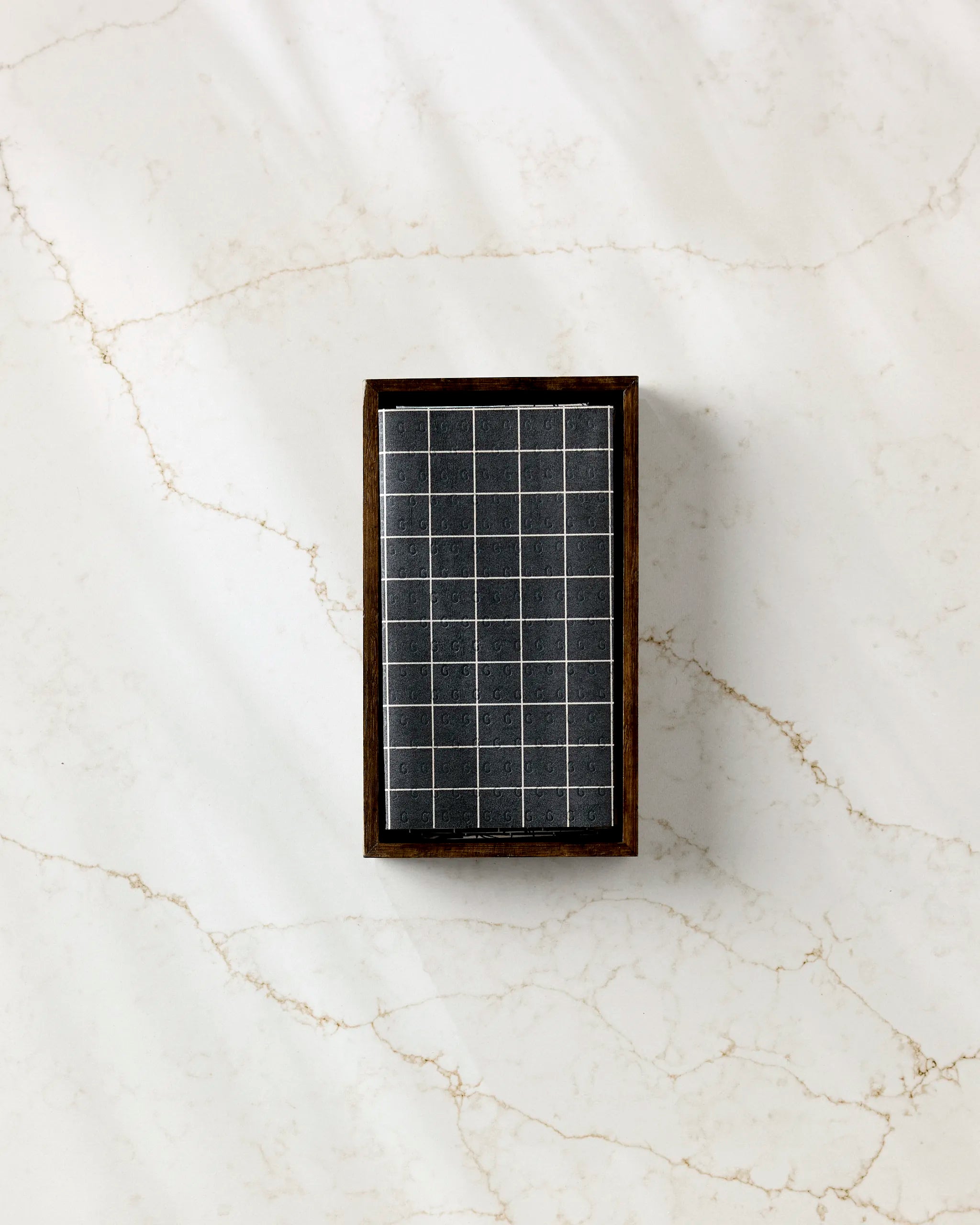 Aubrey Fairchild’s Plant One on Me, a compact rectangular solar panel with water droplets on its surface, rests on light marble with beige veining beside eco-friendly kitchen towels.