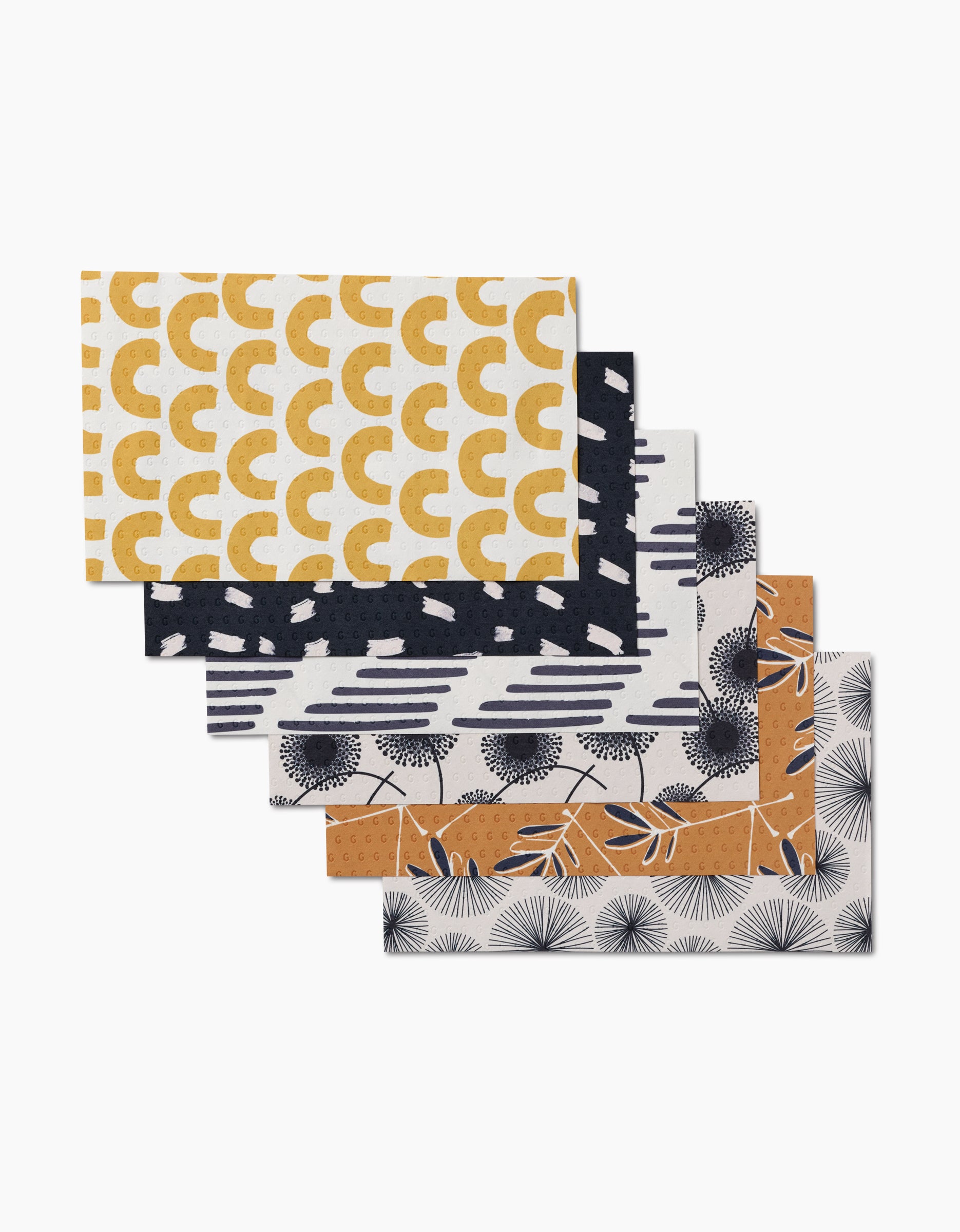 Five rectangular GEOMETRY Pop Of Color dishcloths, each made from post-consumer recycled materials, are fanned out to display unique geometric or botanical patterns in black, mustard yellow, and white.