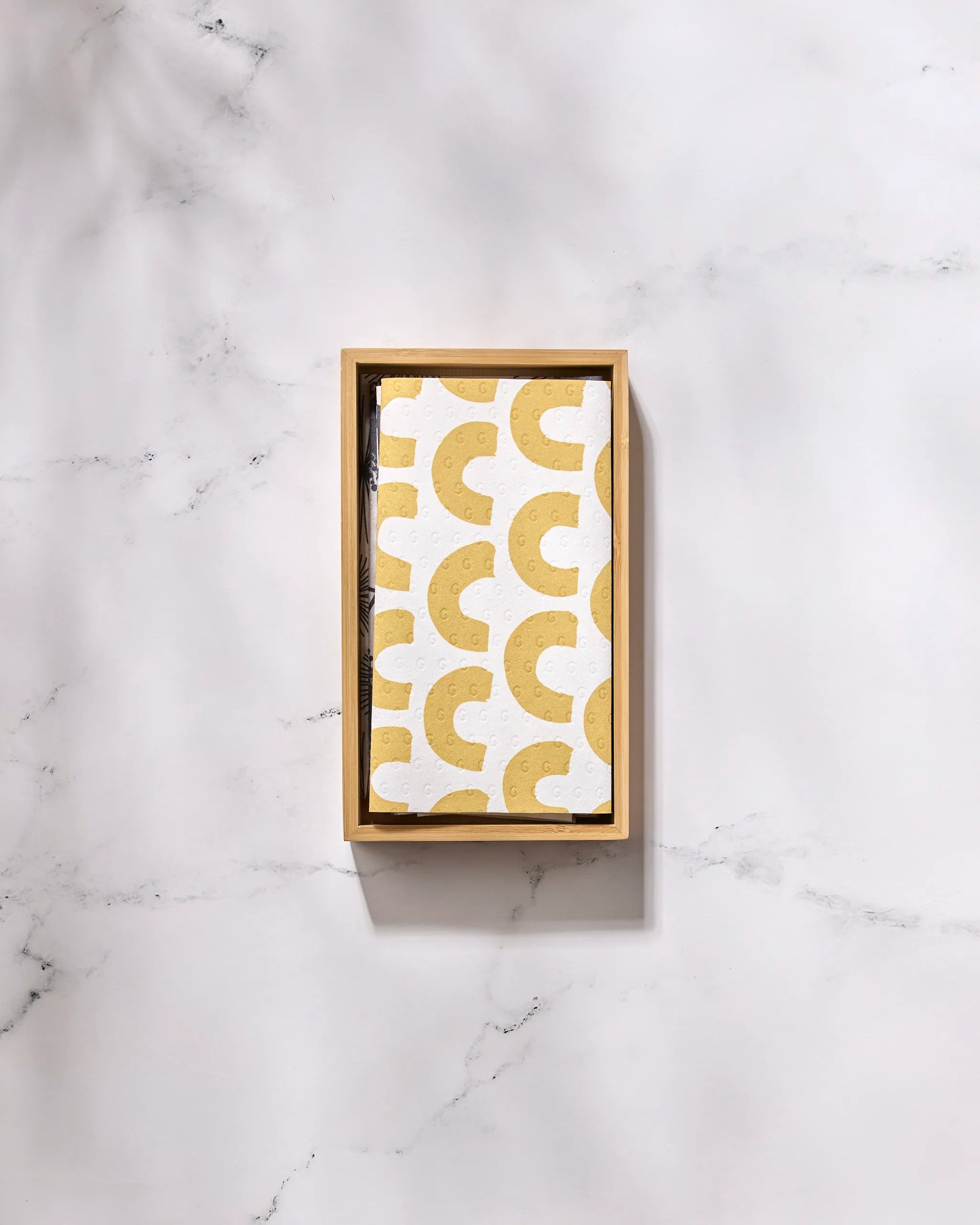 The GEOMETRY Pop Of Color rectangular wooden tray displays a white napkin featuring a repeating yellow crescent pattern, resembling reusable paper towels, resting on a white marble surface.