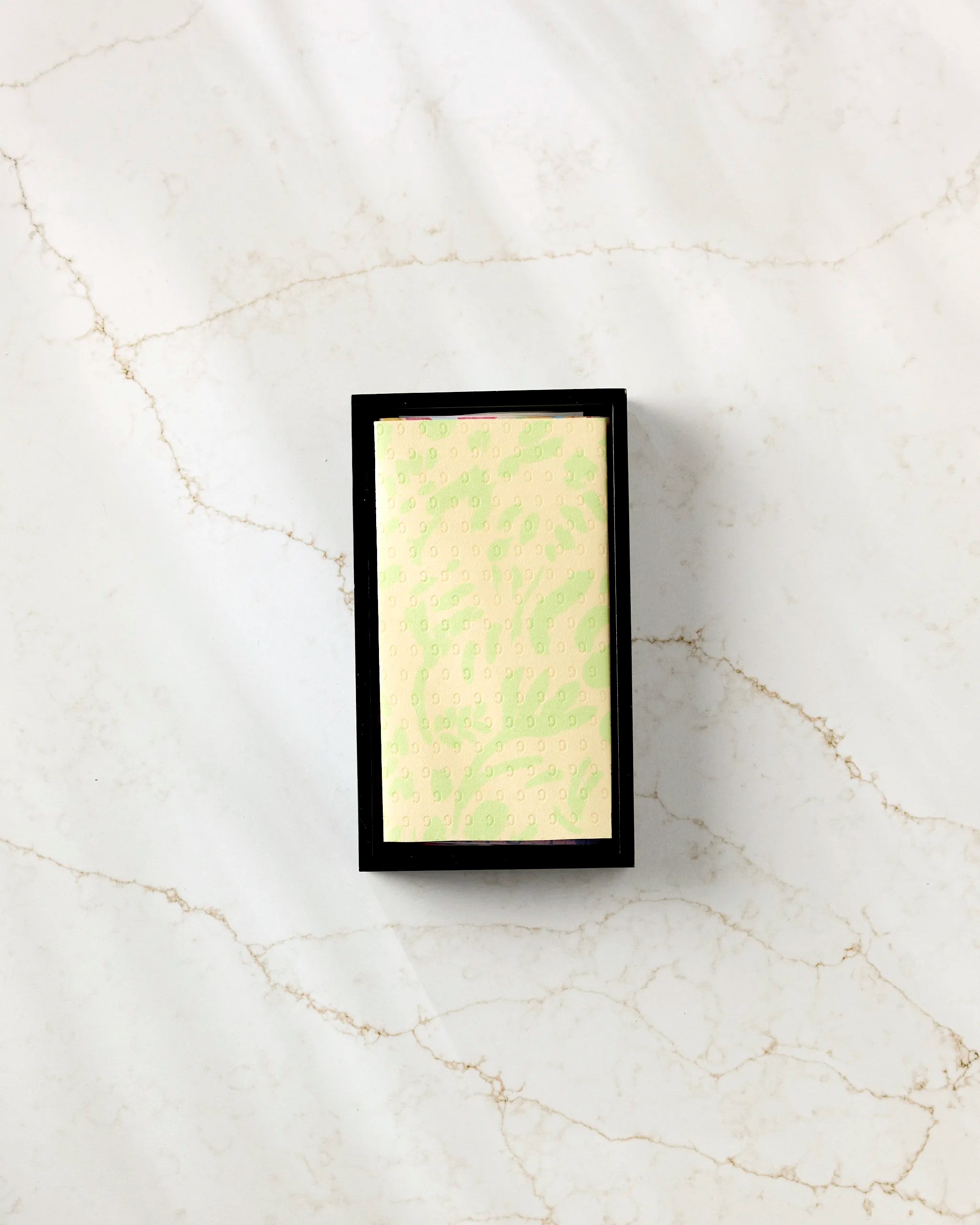 The Positive Vibes bar soap from Sareka Unique, a rectangular pale green bar with an embossed design, rests in a black tray on veined white marble—ideal for pairing with eco-friendly kitchen towels for sustainable style.